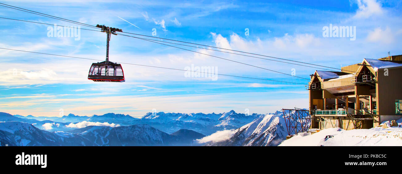 Inverno viaggi montagna vacanze sfondo. Macchina di cavo cabina del tram, stazione di sollevamento, alta montagna di neve picchi e blu cielo nuvoloso Foto Stock