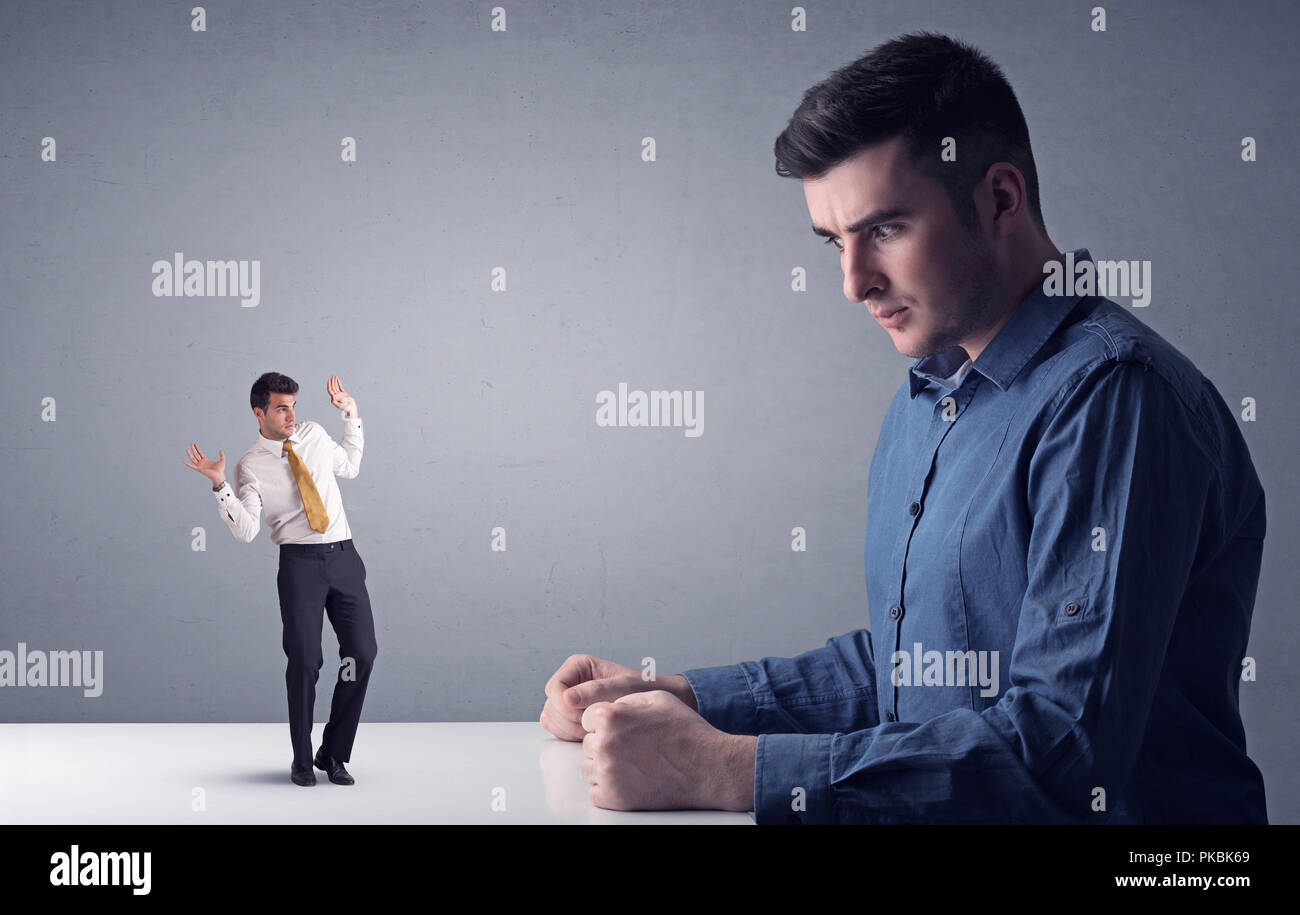 Giovane imprenditore professionale essendo arrabbiato con un altro imprenditore in miniatura di fronte a uno sfondo grigio Foto Stock