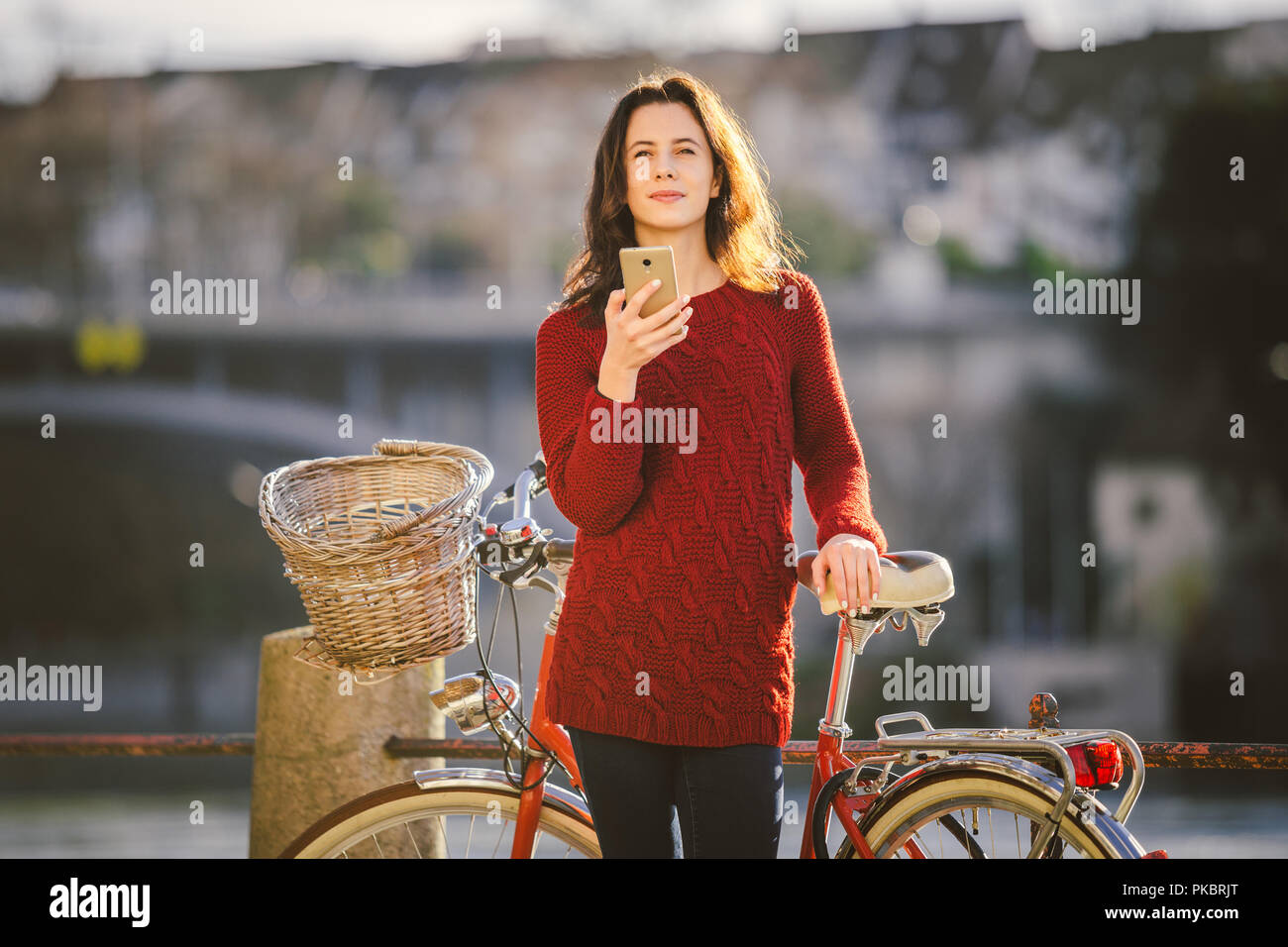 Turismo a tema sulla bicicletta e tecnologia moderna. Bellissima giovane donna caucasica sorge vicino al retro rosso bicicletta sul fiume Reno Basilea Swiss win Foto Stock