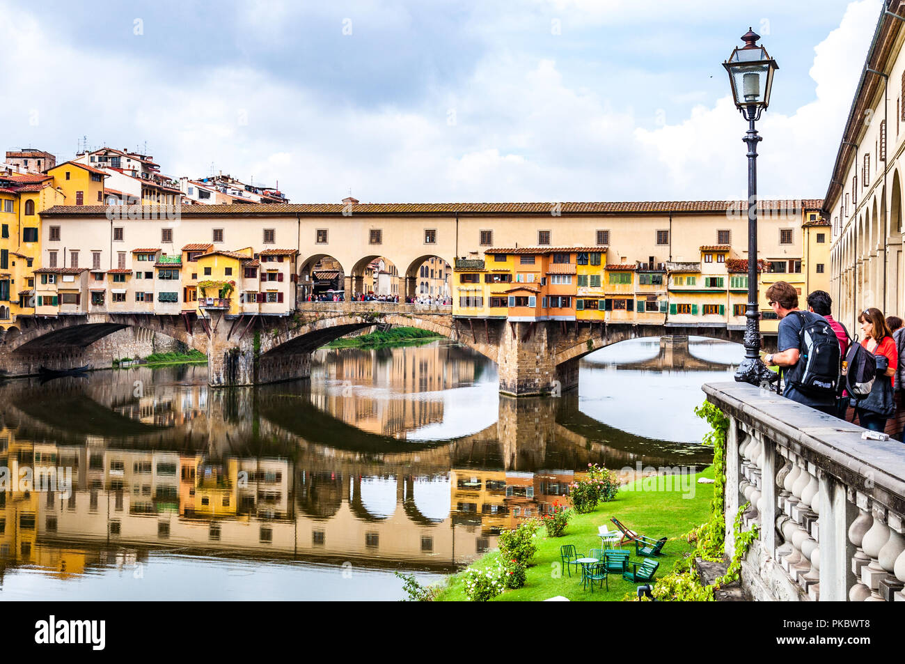 Il Ponte Vecchio sull'Arno con turisti loooking presso di essa e un'erba orlo a Firenze (Firenze), Italia Foto Stock