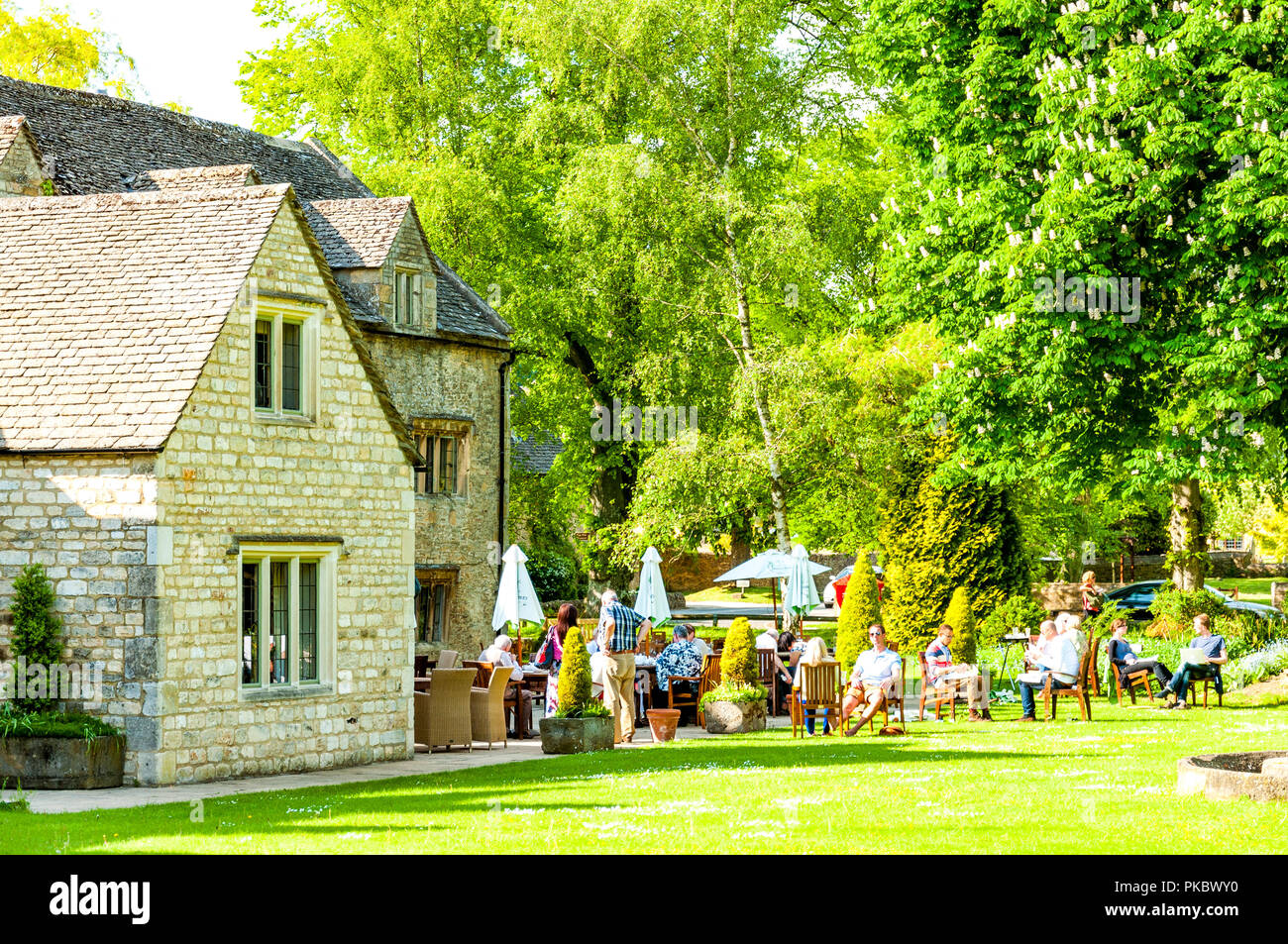 Un paese pub con posti a sedere esterni e le persone e gli alberi del Cotswolds, England, Regno Unito Foto Stock