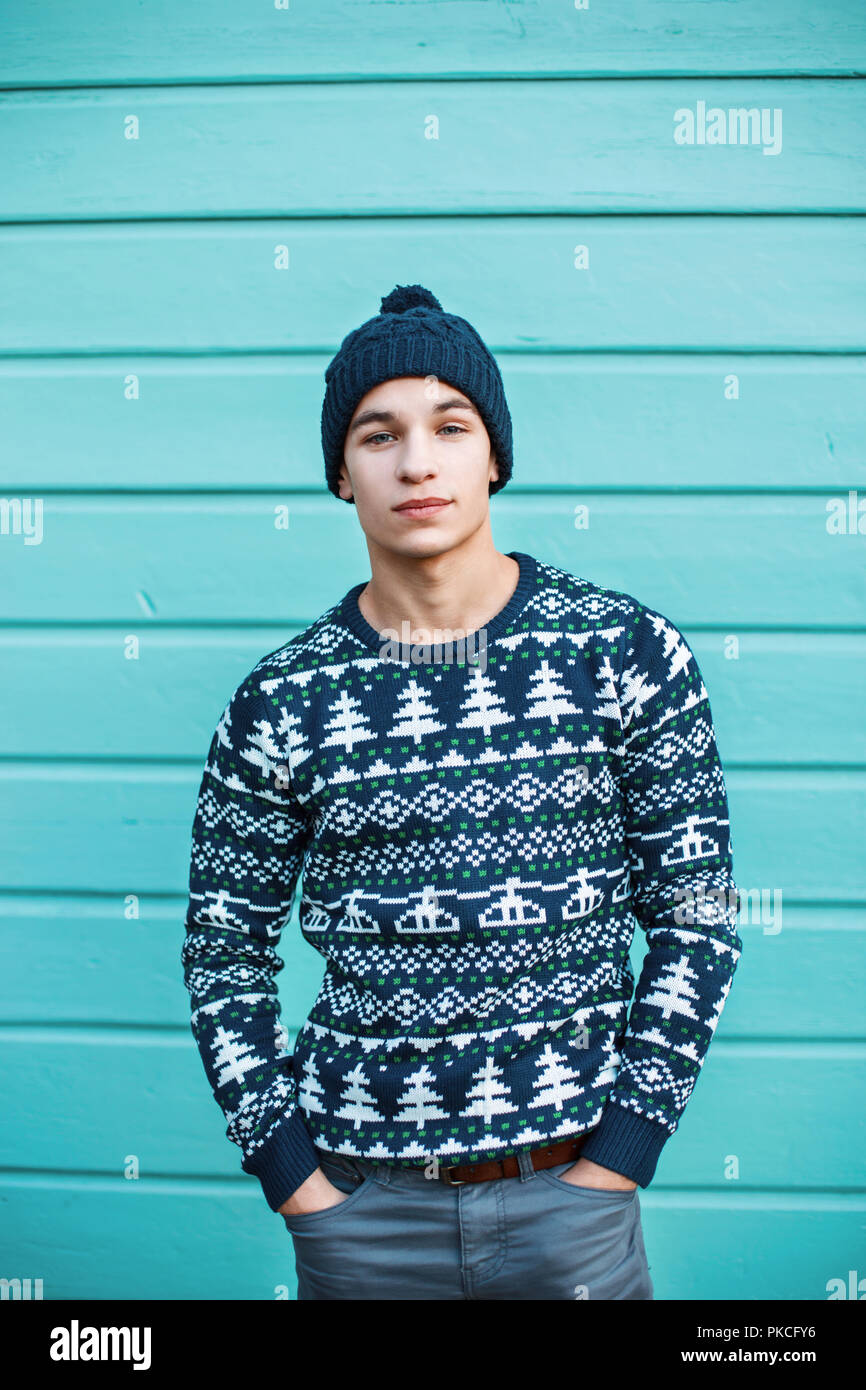 Giovane bello hipster uomo in eleganti vestiti a maglia contro uno sfondo colorato e parete in legno Foto Stock