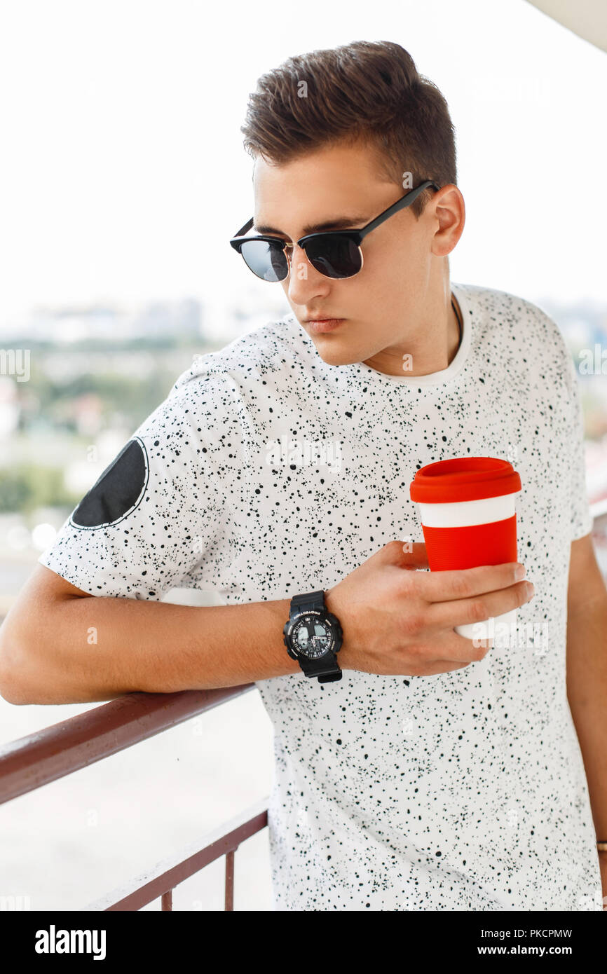 Bello ed elegante hipster Uomo con occhiali da sole tenendo una tazza di caffè Foto Stock