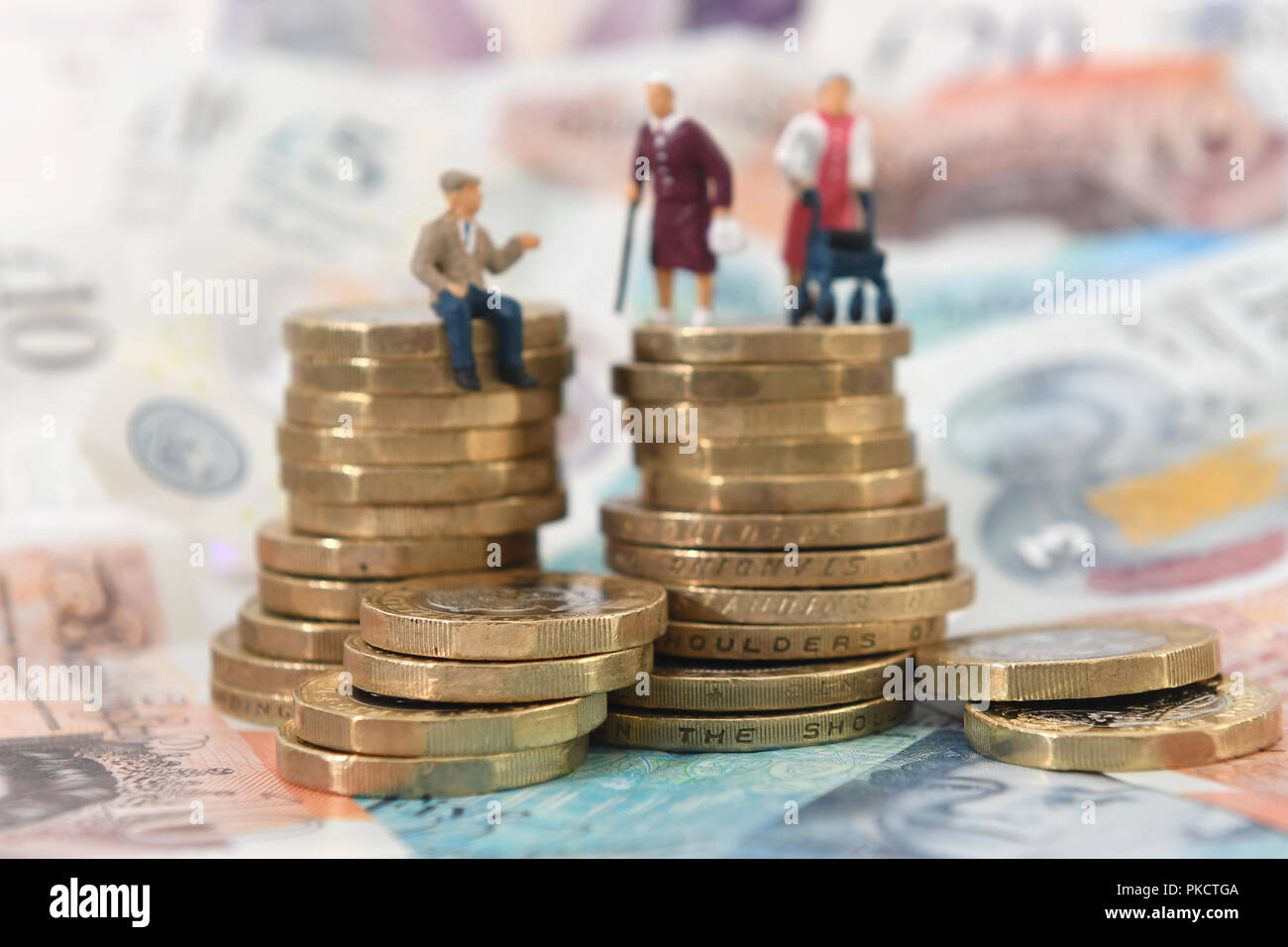 Modelli di anziani su una pila di monete e banconote. Foto Stock