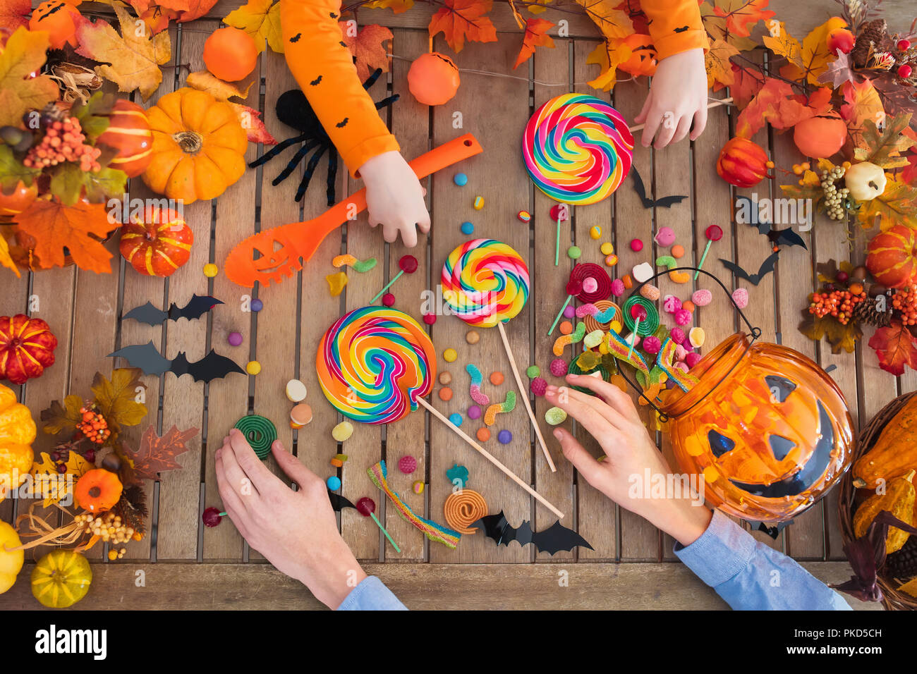 Famiglia con bambino carving zucca di Halloween e mangiare i Trick or Treat candy sul tavolo di legno con foglie di autunno decorazione. Vista superiore piana dei laici kids h Foto Stock