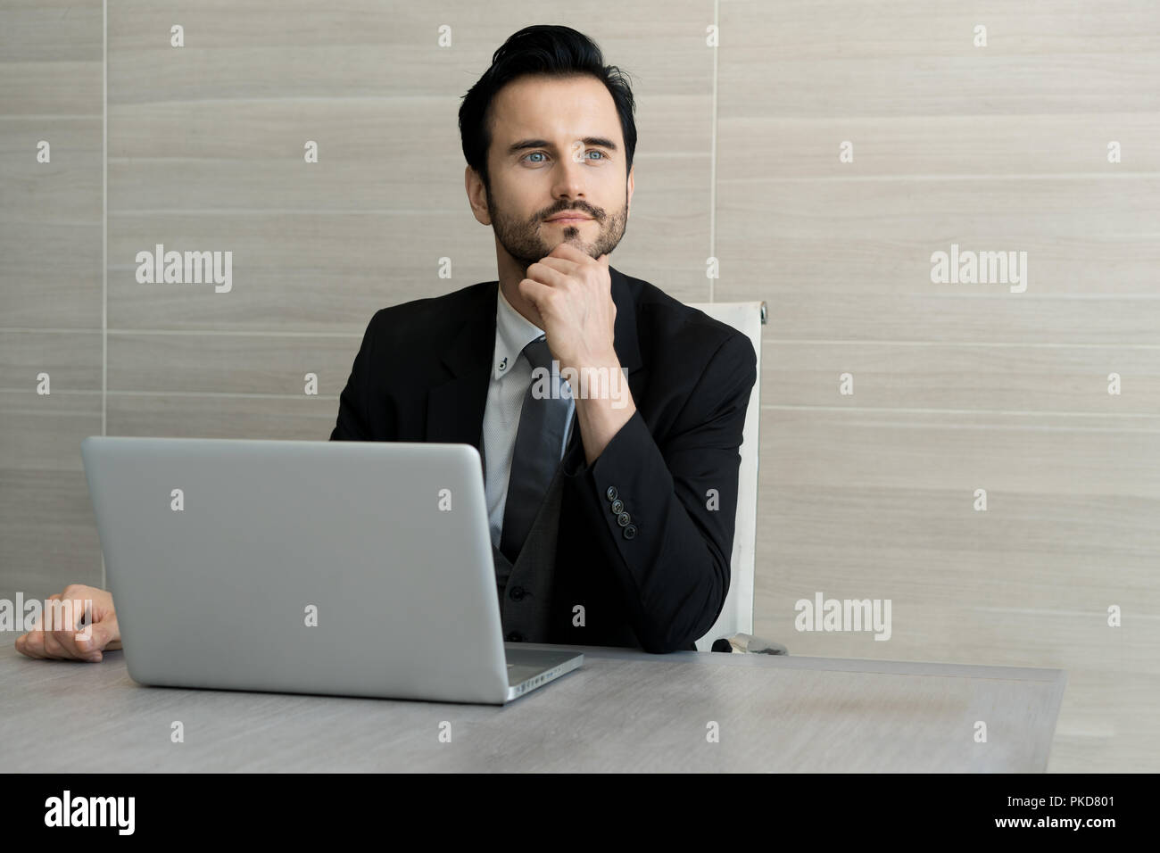 Ritratto di bel giovane azienda uomo seduto in ufficio a lavorare con il computer portatile e il pensiero circa il suo progetto di business. Foto Stock