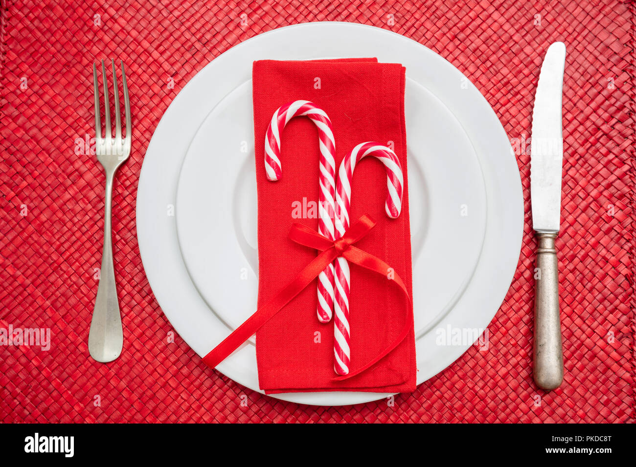 Tavola di natale l'impostazione. Candy canes su bianco piatti e posate, tappeto rosso, vista dall'alto Foto Stock