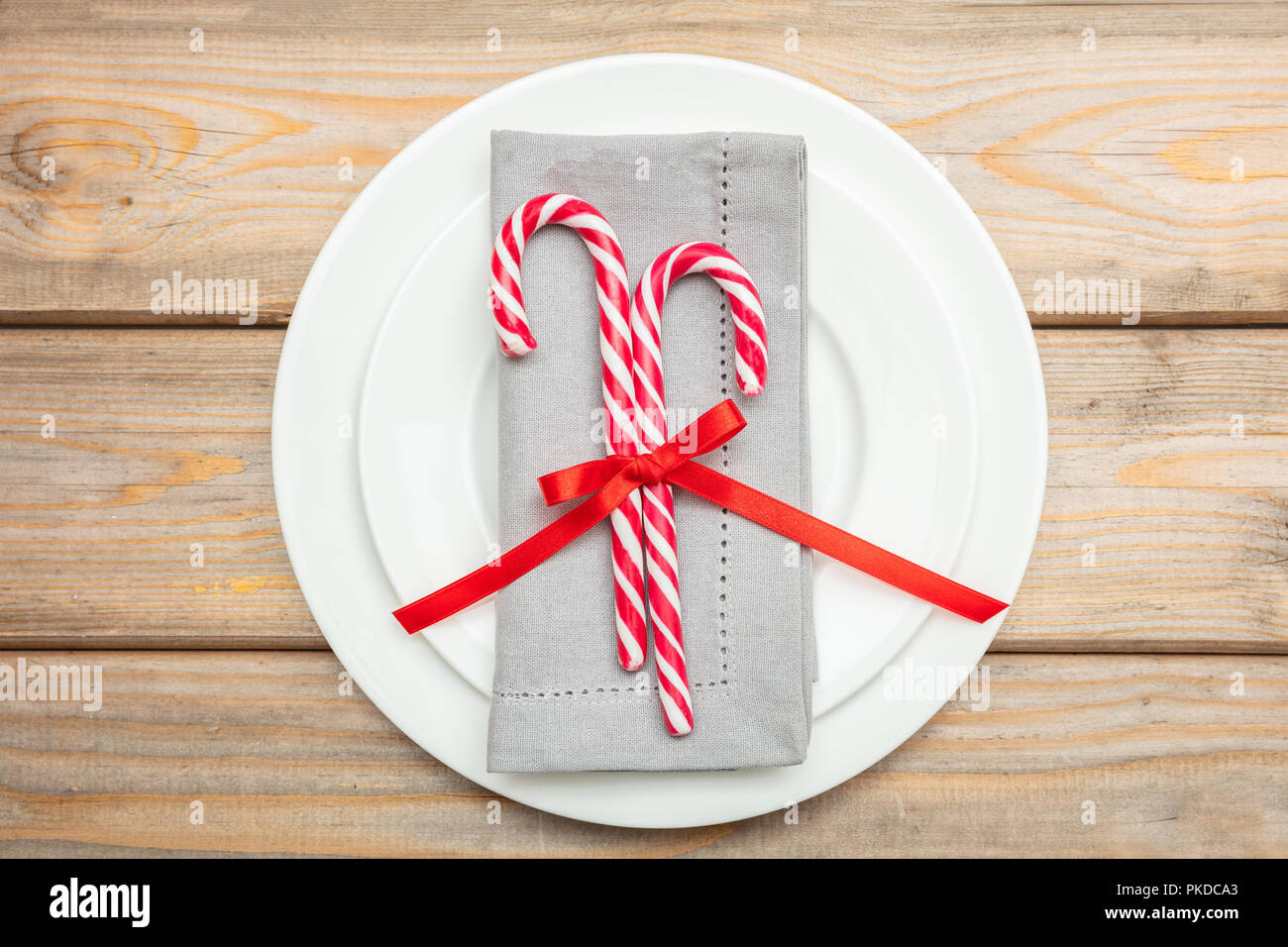 Tavola di natale l'impostazione. Candy canes e grigio di un tovagliolo sulla piastre bianche, sullo sfondo di legno, vista dall'alto Foto Stock
