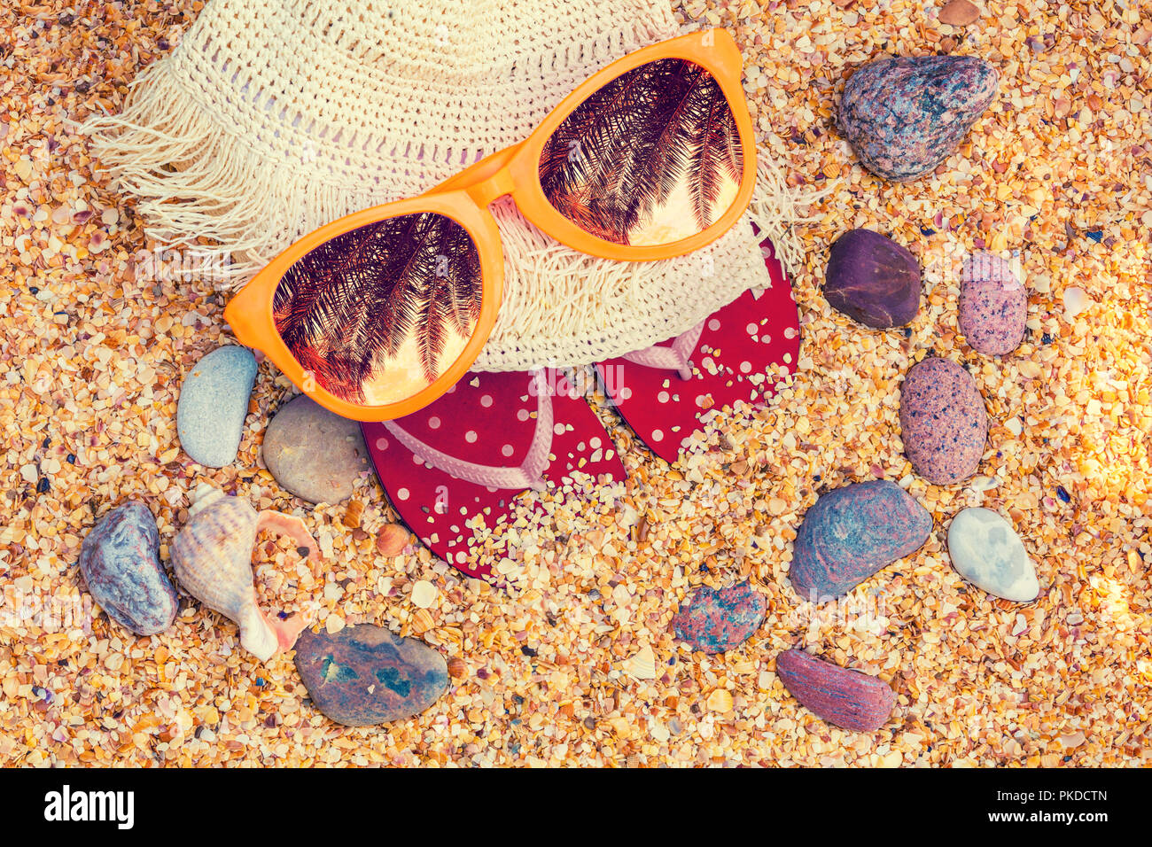 Scena di spiaggia. Sun cappello di paglia, flip-flop sandali e occhiali da sole con Palm tree riflessione giacente sul mare coquina conchiglie sulla spiaggia Foto Stock