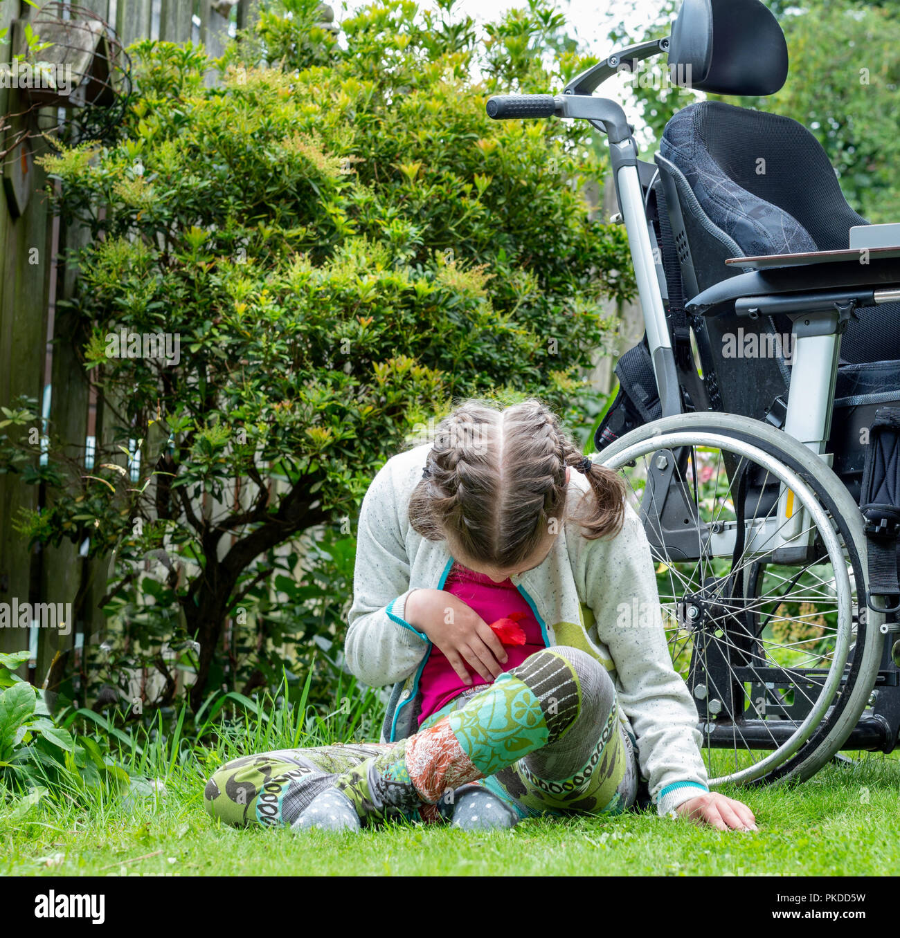 Un bambino disabile avente una pausa dalla seduta nella sua sedia a rotelle per esplorare il suo ambiente naturale Foto Stock