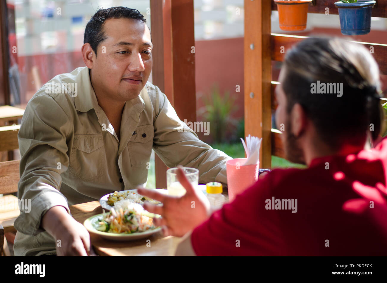 Guardando bene gli uomini a pranzo in un ristorante all'aperto, gli uomini in chat e sorridente Foto Stock