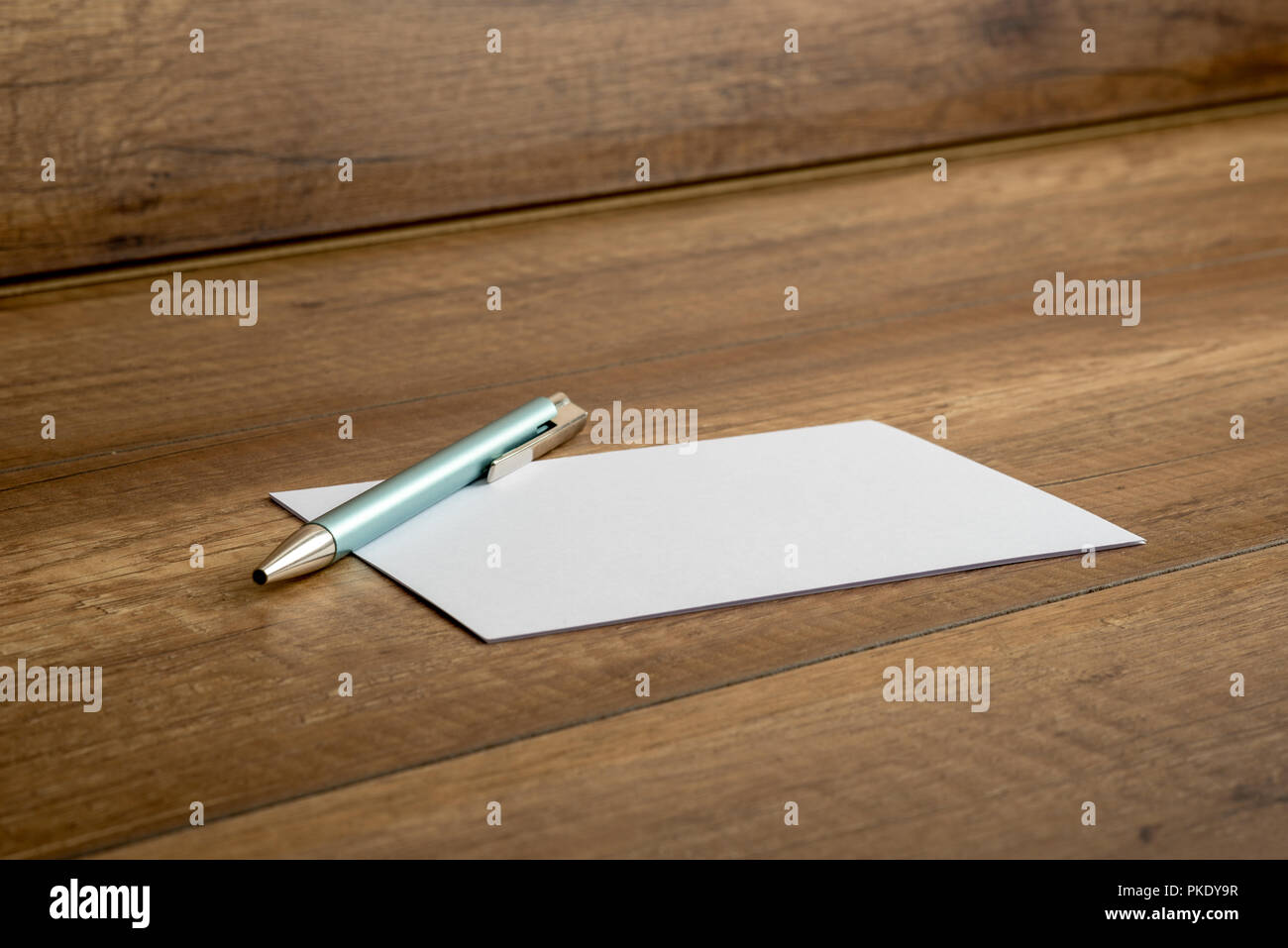 Elegante penna a sfera e il vuoto di carta bianca o di una nota che giace su di un tavolo di legno, basso angolo vista obliqua. Foto Stock