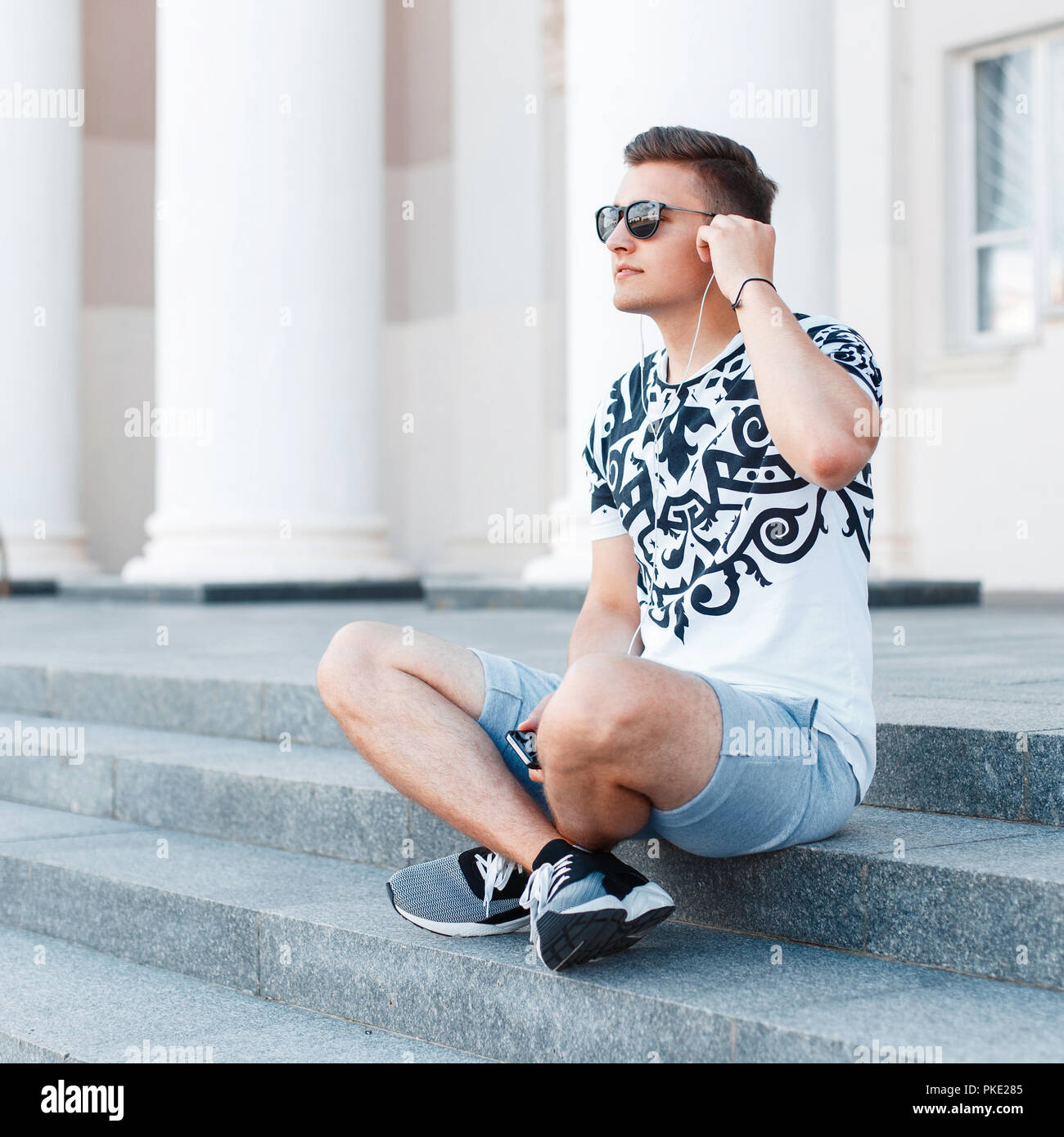 Giovane uomo elegante con occhiali da sole seduti sulle scale e ascolto di musica. Foto Stock