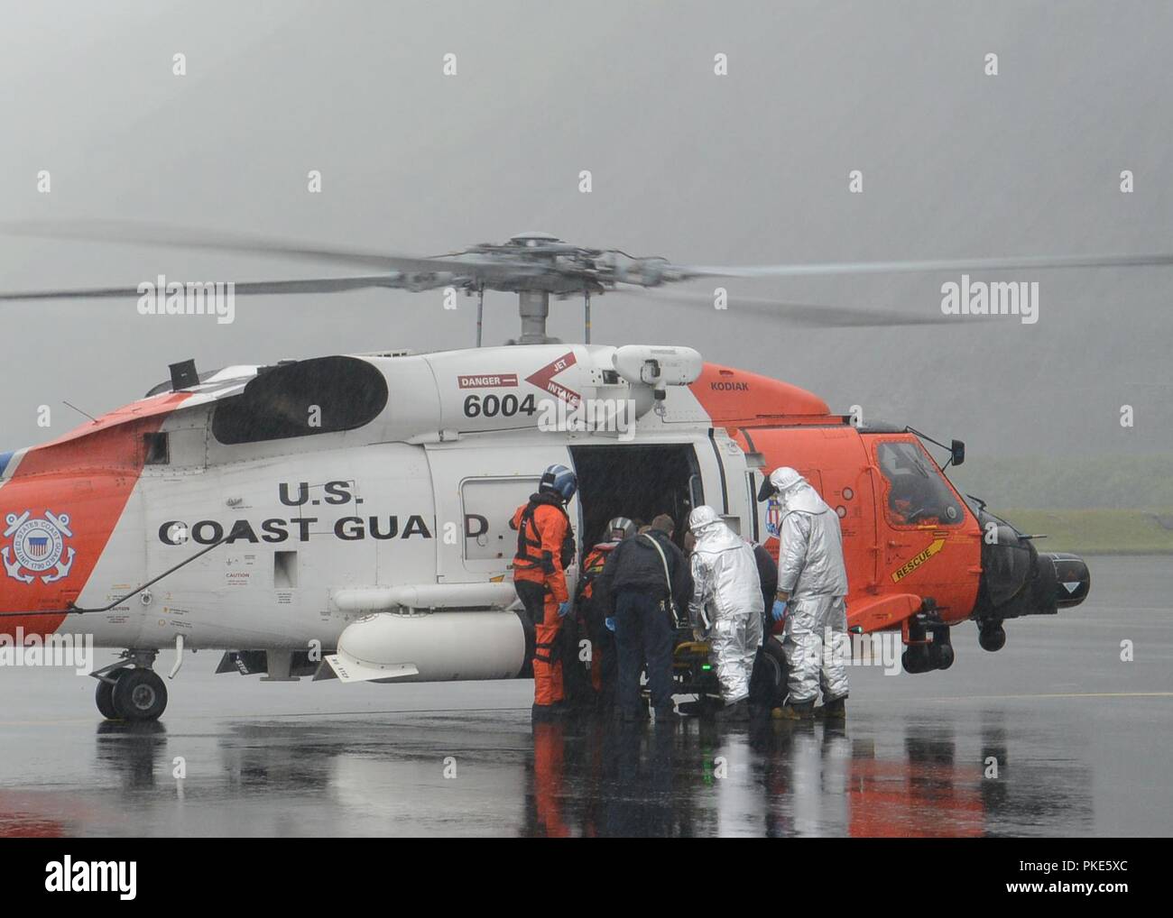 Una guardia costiera Stazione aria Kodiak Jayhawk equipaggio, Base Kodiak fire personale di reparto e la città di Kodiak emergenza personale medico preparare per il trasferimento di un 47-anno-vecchio uomo per un ambulanza in attesa presso la stazione aerea di Kodiak, Alaska, 25 luglio 2018. L'uomo subito un infortunio alla gamba sulla nave da pesca Sci nordico 20 miglia a nord di Kodiak. Stati Uniti Coast Guard Foto Stock