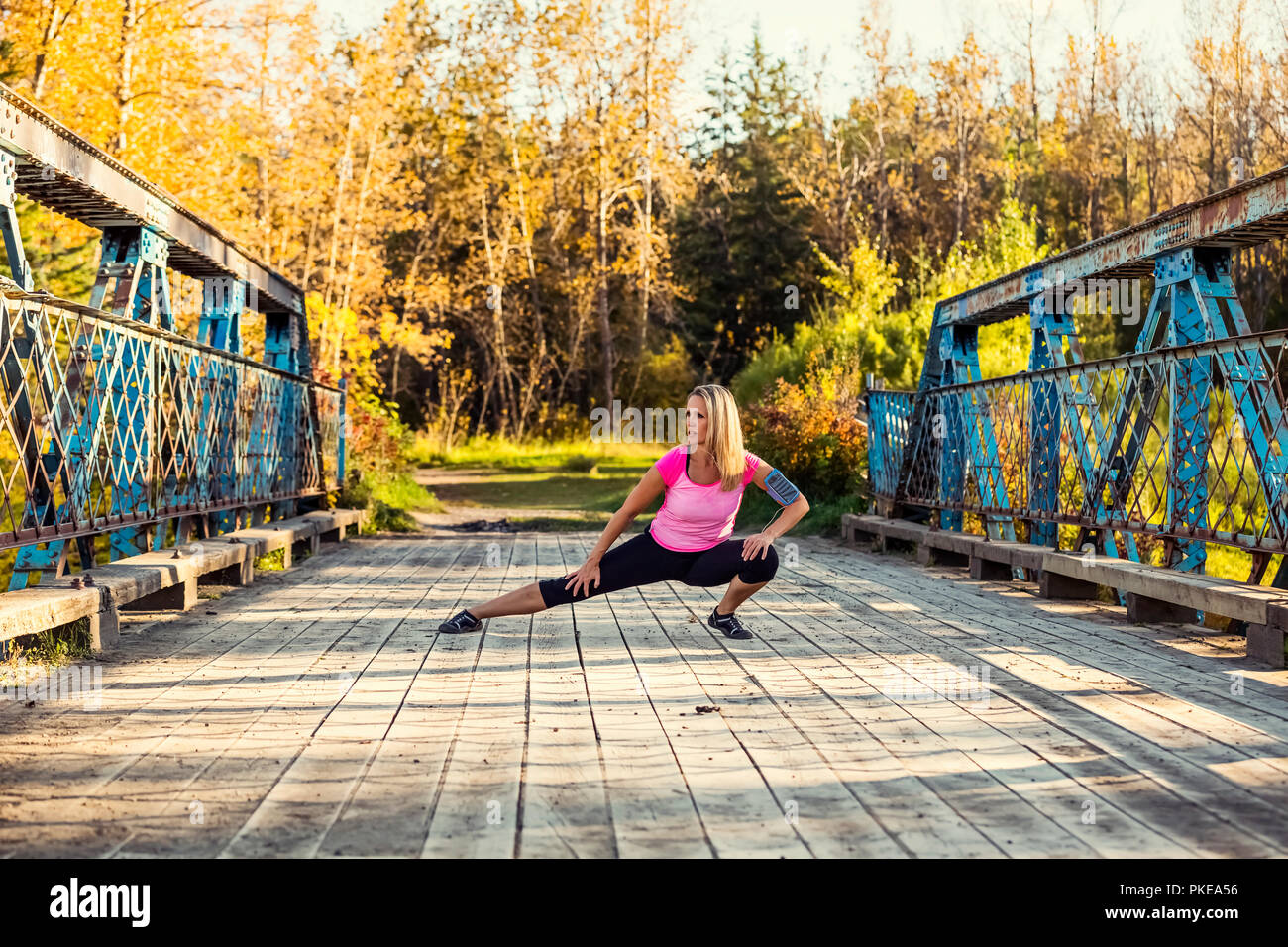Un attraente donna di mezza età delle pause per tendere le sue gambe su un ponte durante una corsa su un bellissimo autunno caldo la sera in un parco della città Foto Stock