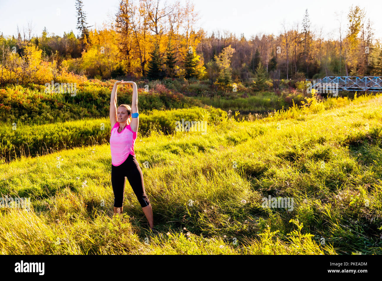 Una donna di mezza età attraente che indossa abbigliamento attivo e ascolta musica mentre si fa una pausa per fare alcuni esercizi di stretching durante una corsa in un parco... Foto Stock