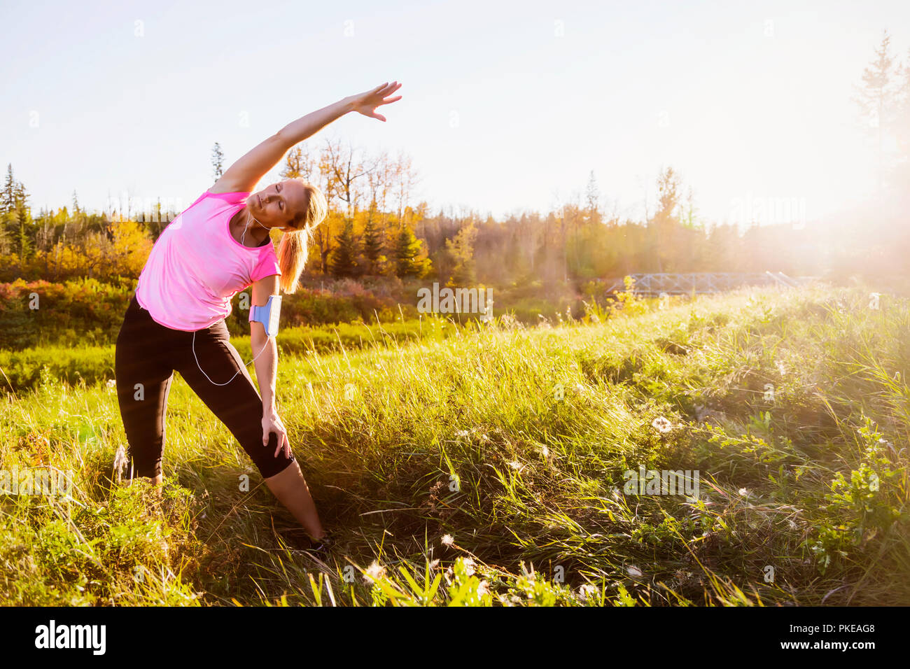 Una donna di mezza età attraente che indossa abbigliamento attivo e ascolta musica mentre si fa una pausa per fare alcuni esercizi di stretching durante una corsa in un parco... Foto Stock