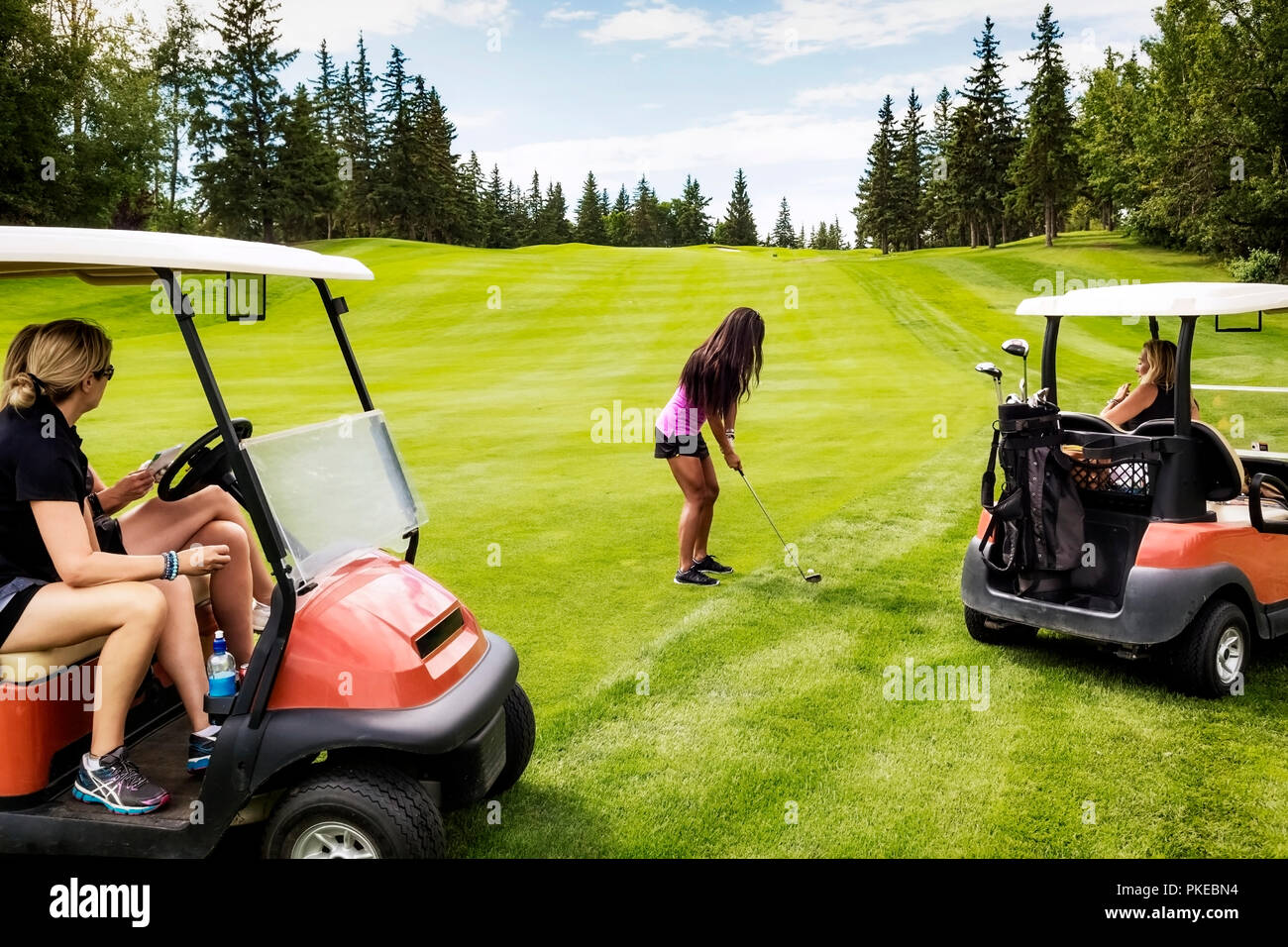 Un gruppo di golfers femminili che guardano dai loro carrelli di golf mentre il loro compagno di squadra sta progettando il suo colpo fuori del grezzo su un campo di golf su un summ... Foto Stock