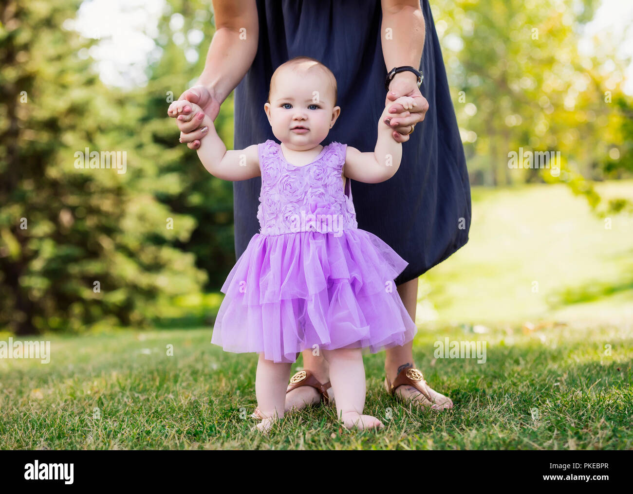 Una madre insegnare la sua bimba come andare a piedi in un parco cittadino in un caldo pomeriggio di caduta: Edmonton, Alberta, Canada Foto Stock