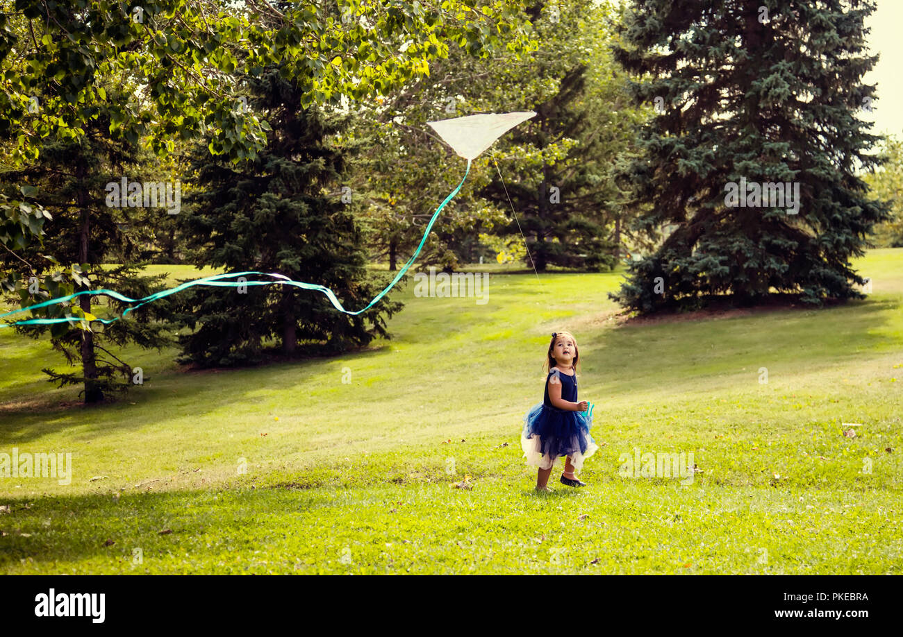 Una giovane ragazza in un abito in esecuzione e volare un aquilone in un parco cittadino in un caldo pomeriggio di caduta; Edmonton, Alberta, Canada Foto Stock