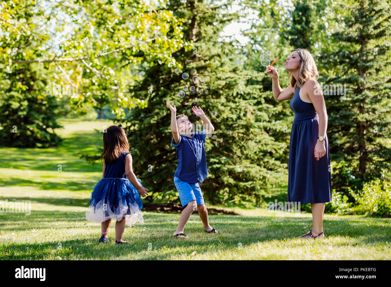 Una madre a soffiare bolle per i suoi bambini durante una gita di famiglia in un parco in una calda giornata di caduta; Edmonton, Alberta, Canada Foto Stock