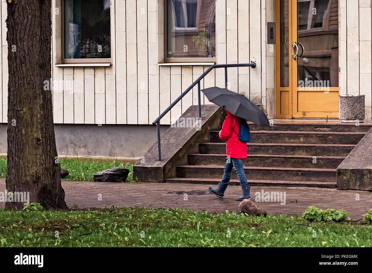 Un bambino a piedi con un grande ombrellone e un rosso cappotto di pioggia in un giorno di primavera a Tallinn in Estonia. Foto Stock