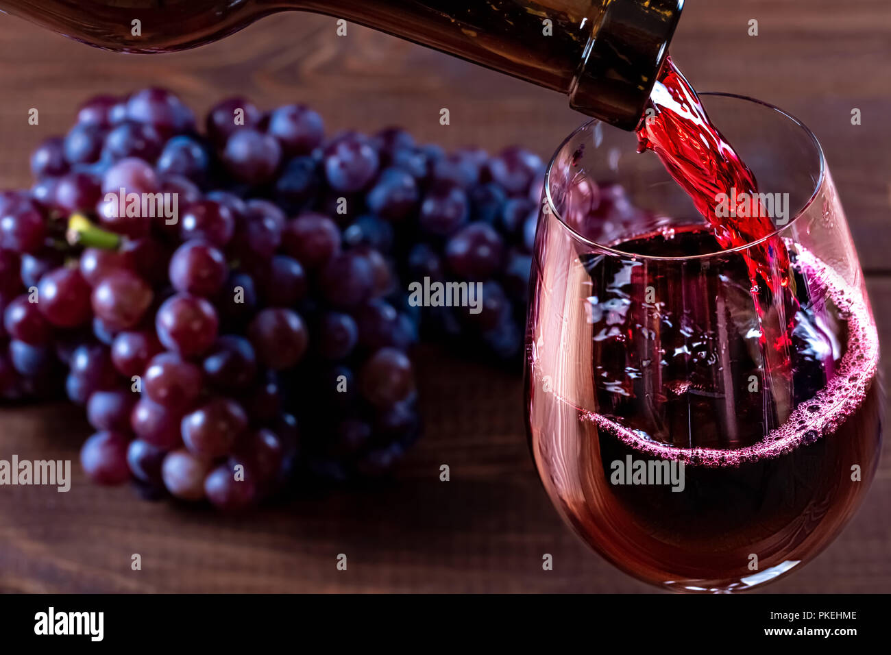 Bottiglia e bicchiere di vino rosso, uva e sughero su sfondo di legno Foto Stock