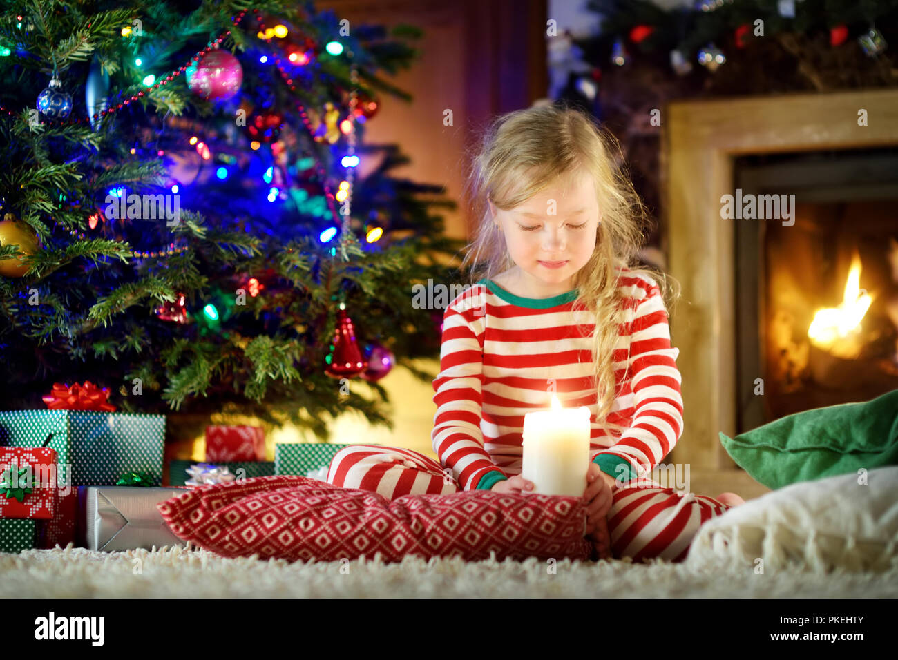 Felice bambina indossa pigiami di Natale la riproduzione da un camino in un buio accogliente soggiorno alla vigilia di Natale. Celebrare il Natale a casa. Foto Stock