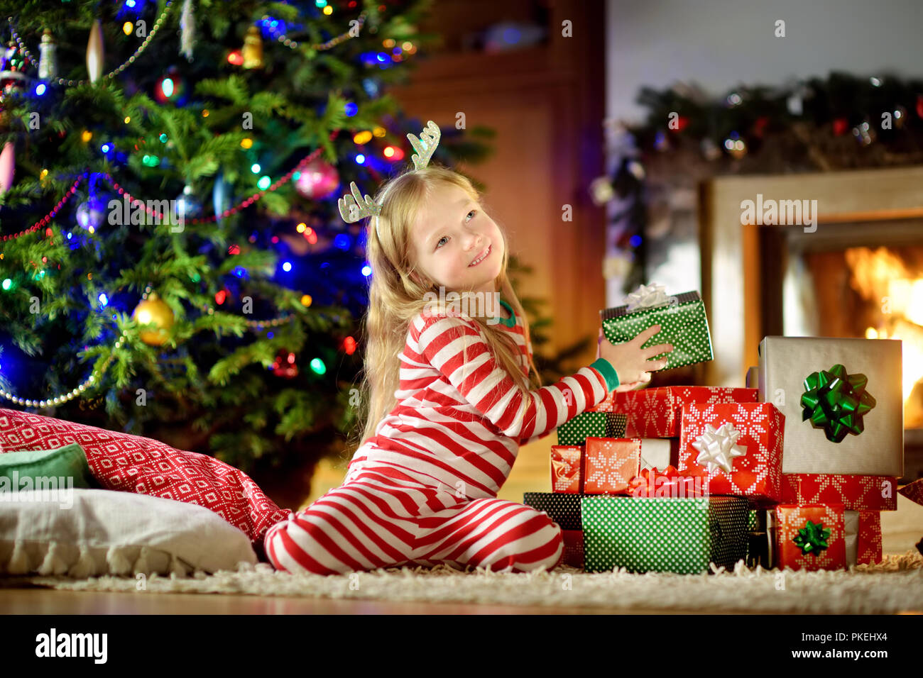 Felice bambina indossa pigiami di Natale la riproduzione da un camino in un buio accogliente soggiorno alla vigilia di Natale. Celebrare il Natale a casa. Foto Stock