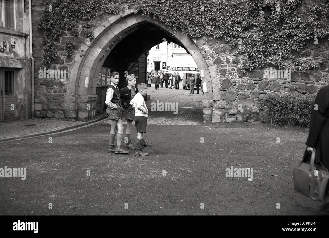Degli anni Cinquanta, storico, Colonia, Germania, tre ragazzi indossando il tradizionale tedesco pantaloncini in pelle o lederhosen, assieme al di fuori di un ingresso ad arco al centro storico della città. Foto Stock