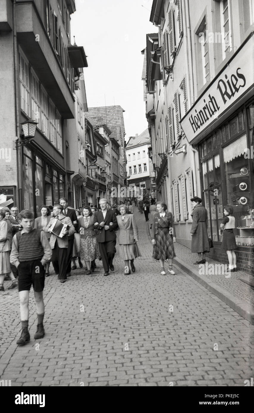 Degli anni Cinquanta, storico, Colonia, Germania, un piccolo gruppo di persone che camminano giù una stretta strada di ciottoli nel centro storico della città di canto, guardato dalla Madonna e Bambino in piedi al di fuori del negozio di jewlery di Heinrich Ries. Gran parte del centro città è stata distrutta durante il WW2 e dovette essere ricostruita. Foto Stock