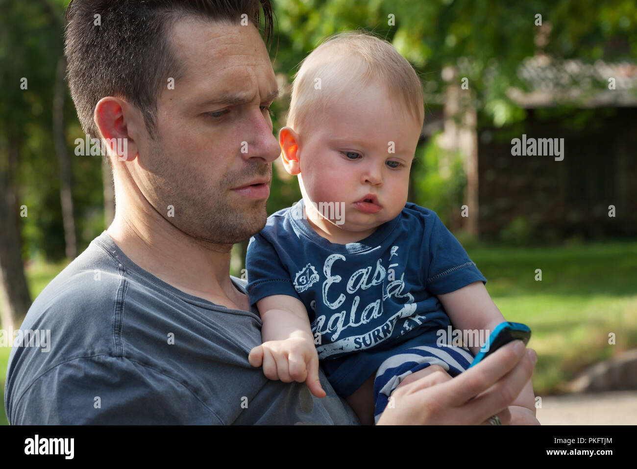 Padre e figlio guardando un telefono cellulare avente fun - genitore single e 13 mesi baby godendo all'aperto Foto Stock