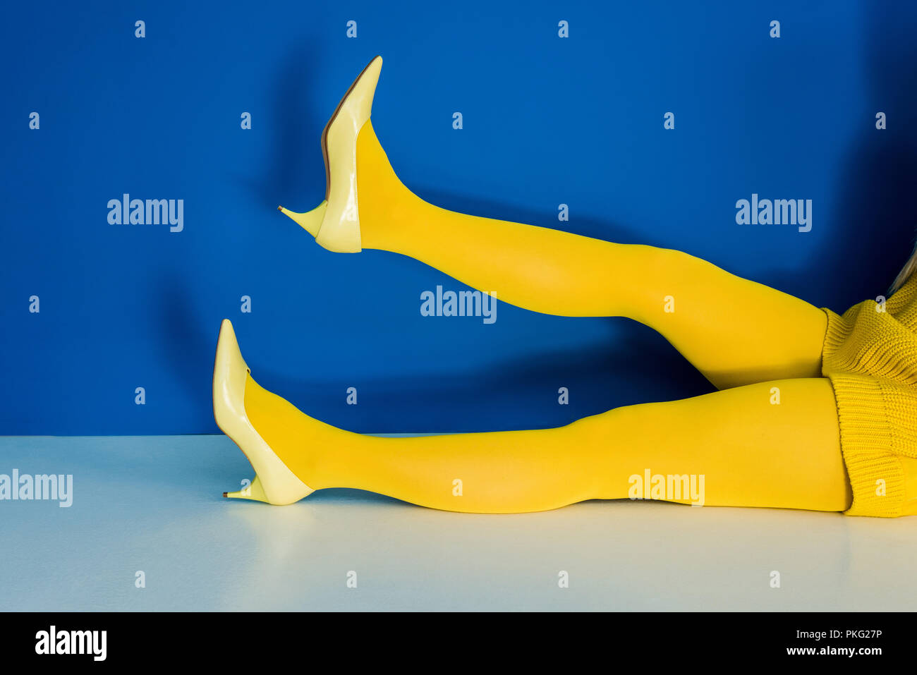Vista ritagliata della gambe femmina in giallo le scarpe e collant su sfondo blu Foto Stock