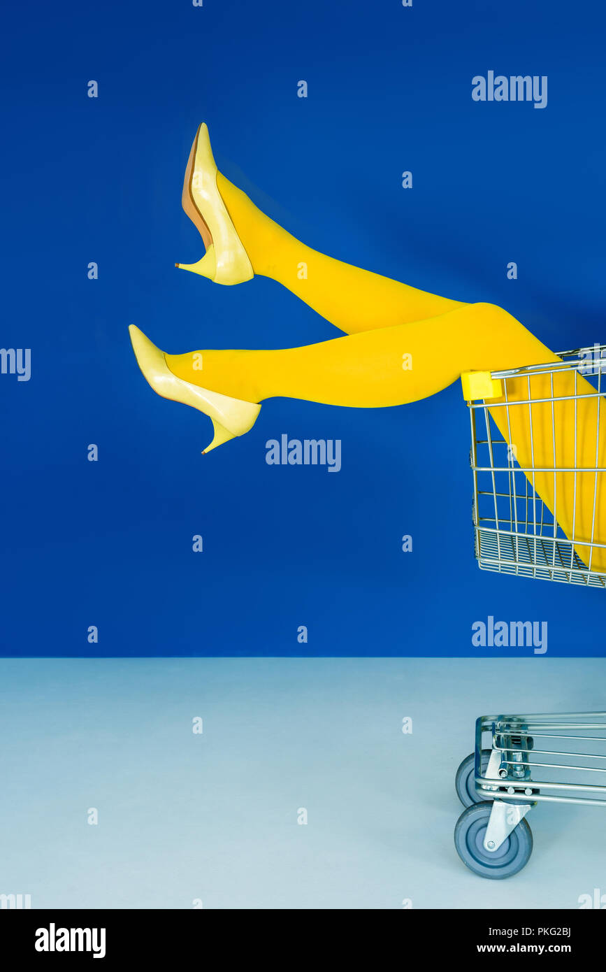 Vista ritagliata della gambe femmina nel carrello su sfondo blu Foto Stock