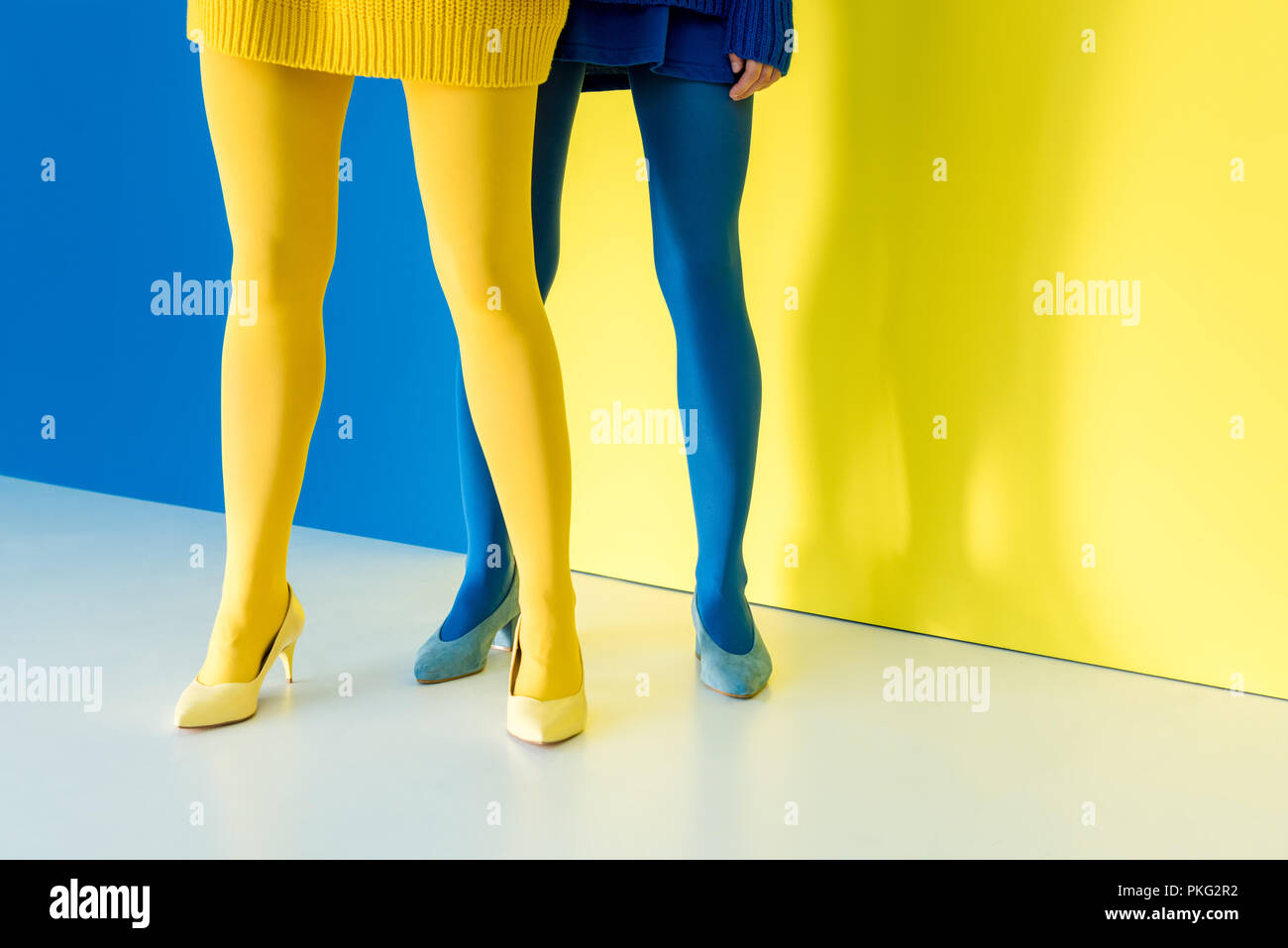 Vista ritagliata della gambe femminile in blu e giallo sul collant blu e sfondo giallo Foto Stock