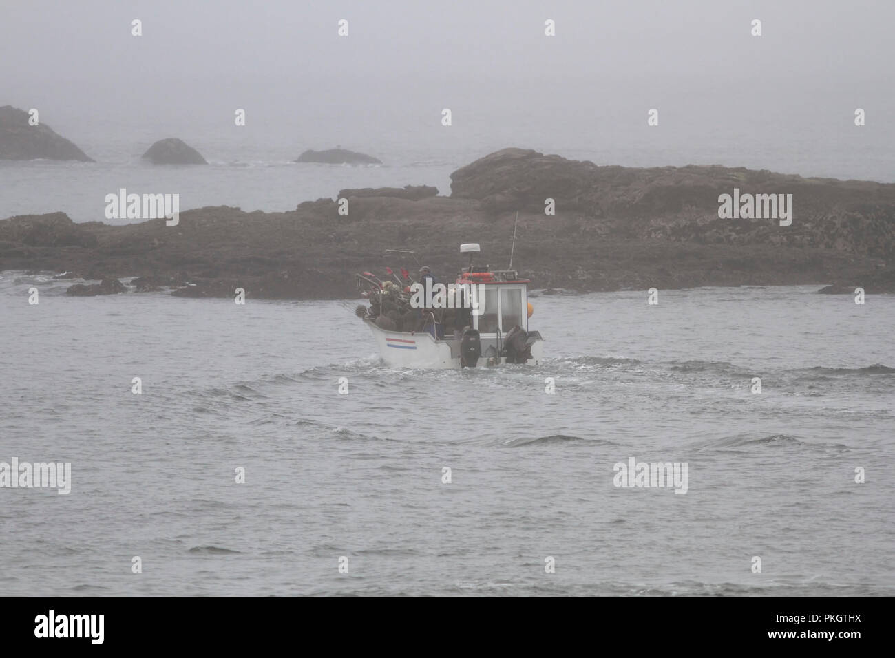 Portoghese tradizionale piccola barca da pesca durante la fatica tra massi. Portoghese settentrionale costa rocciosa in un estate mattinata nebbiosa. Foto Stock