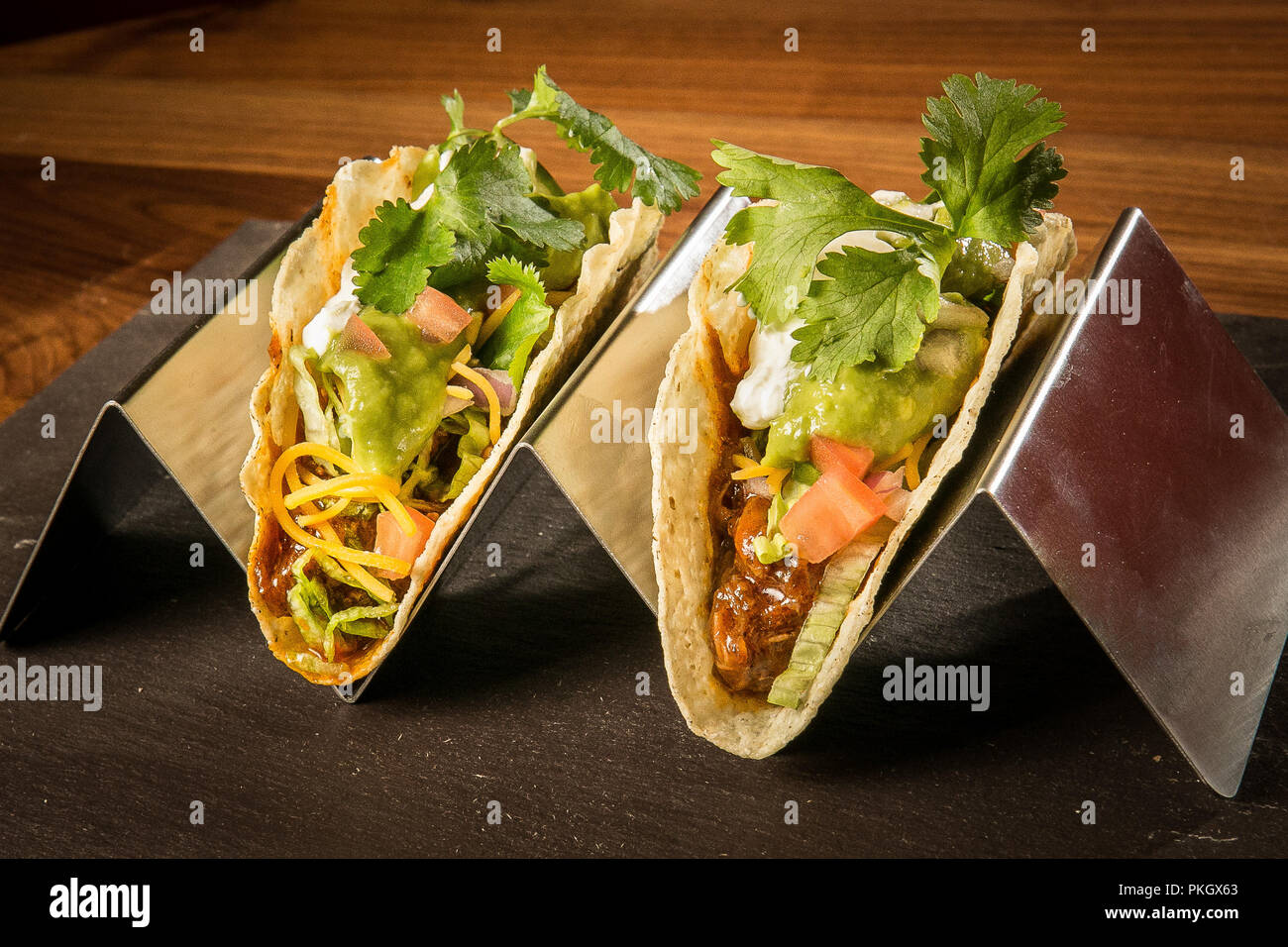 Tirate la carne di maiale Taco su un acciaio inox stand con uno sfondo rosso su una superficie in pietra e legno tavolo. Fotografia di Arpi Pap Foto Stock