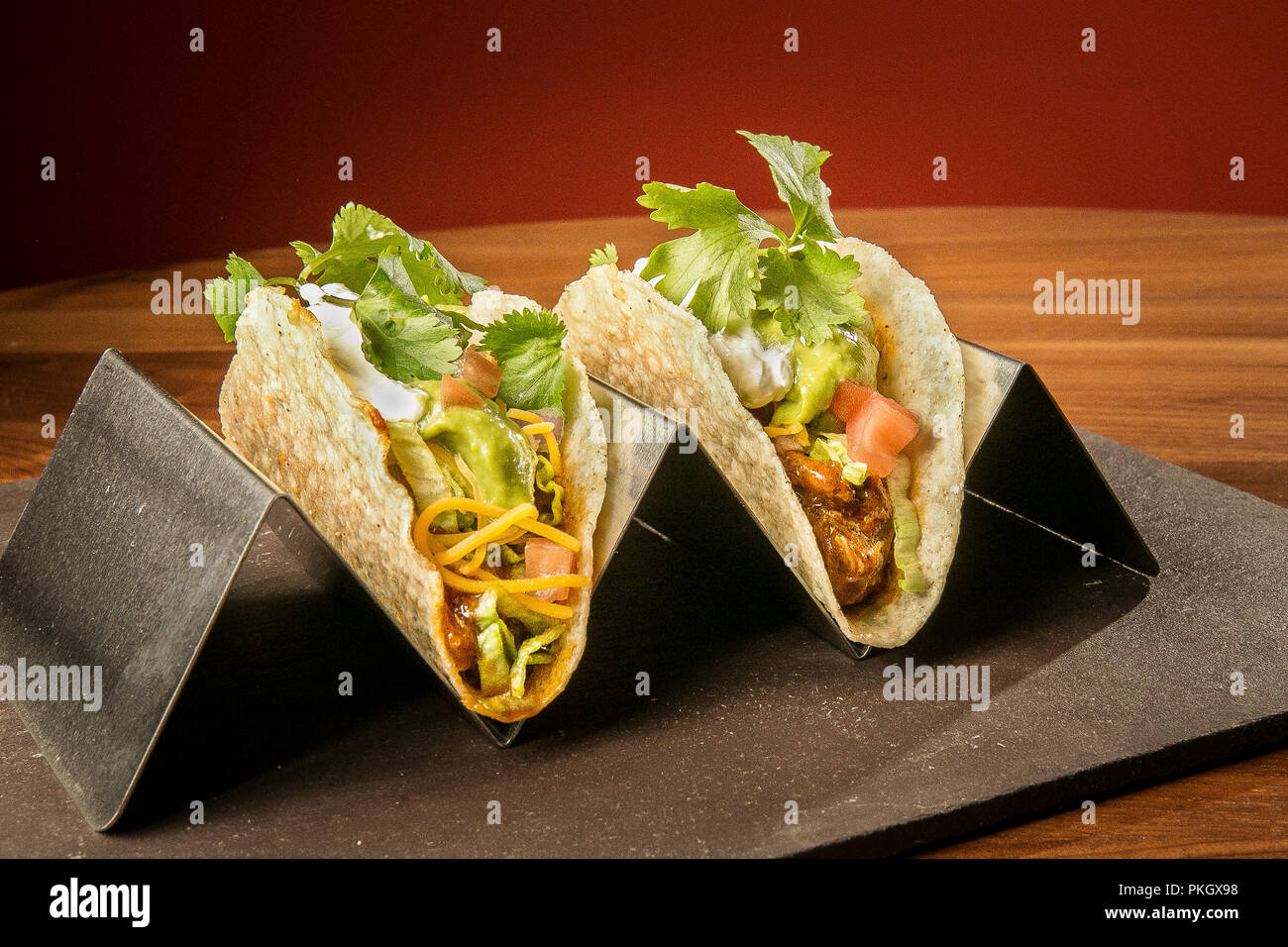 Tirate la carne di maiale Taco su un acciaio inox stand con uno sfondo rosso su una superficie in pietra e legno tavolo. Fotografia di Arpi Pap Foto Stock