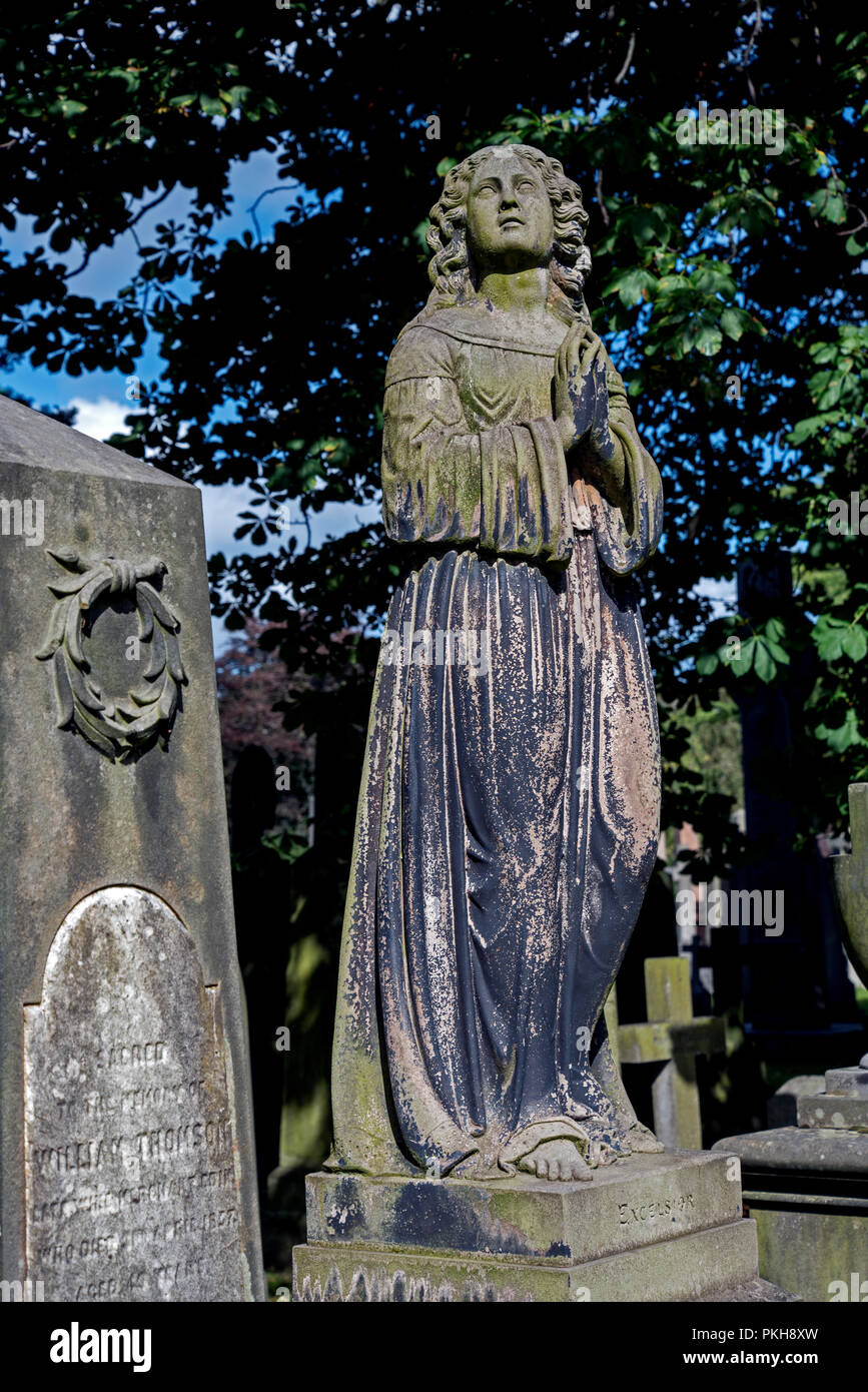 Victorian statua di una donna con le mani giunte in preghiera contro uno sfondo di alberi nel cimitero di Dean, Edimburgo. Foto Stock