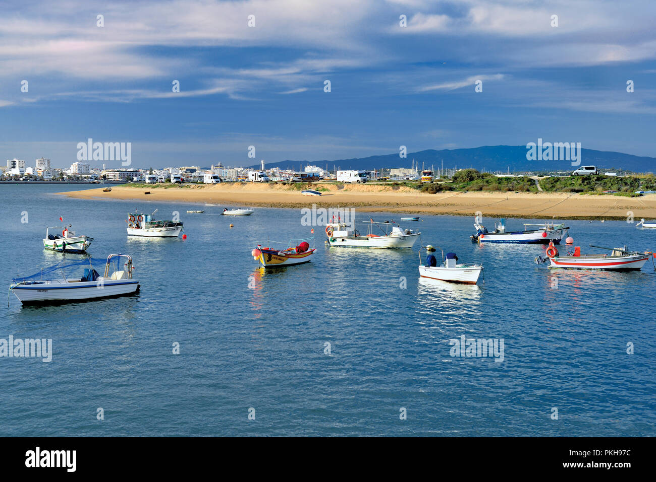 Barche da pesca di ancoraggio nel estuario del fiume con sandbank, verde collina e città in background Foto Stock