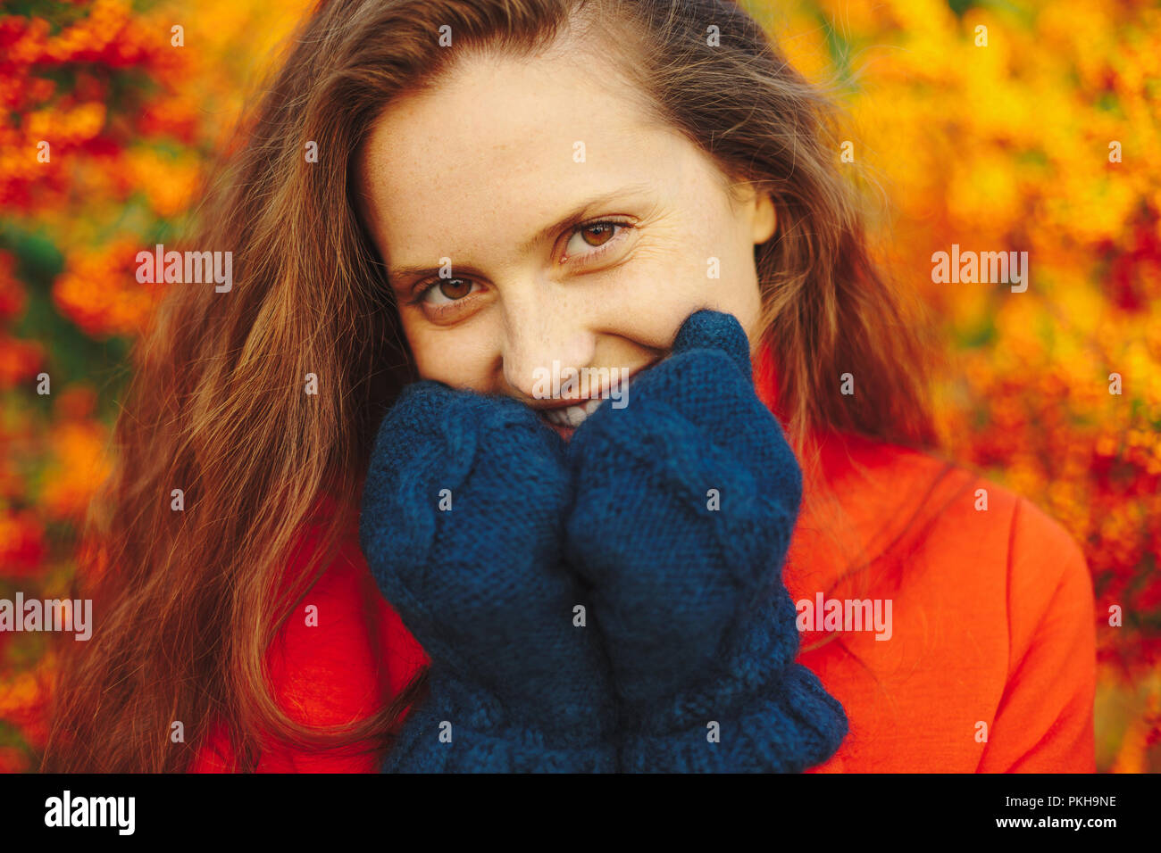 Close-up ritratto di una giovane donna sorridente in rosso cappotto e navy guanti invernali su frutti di bosco sfondo. Bella ragazza naturale con lunghi capelli ondulati Foto Stock