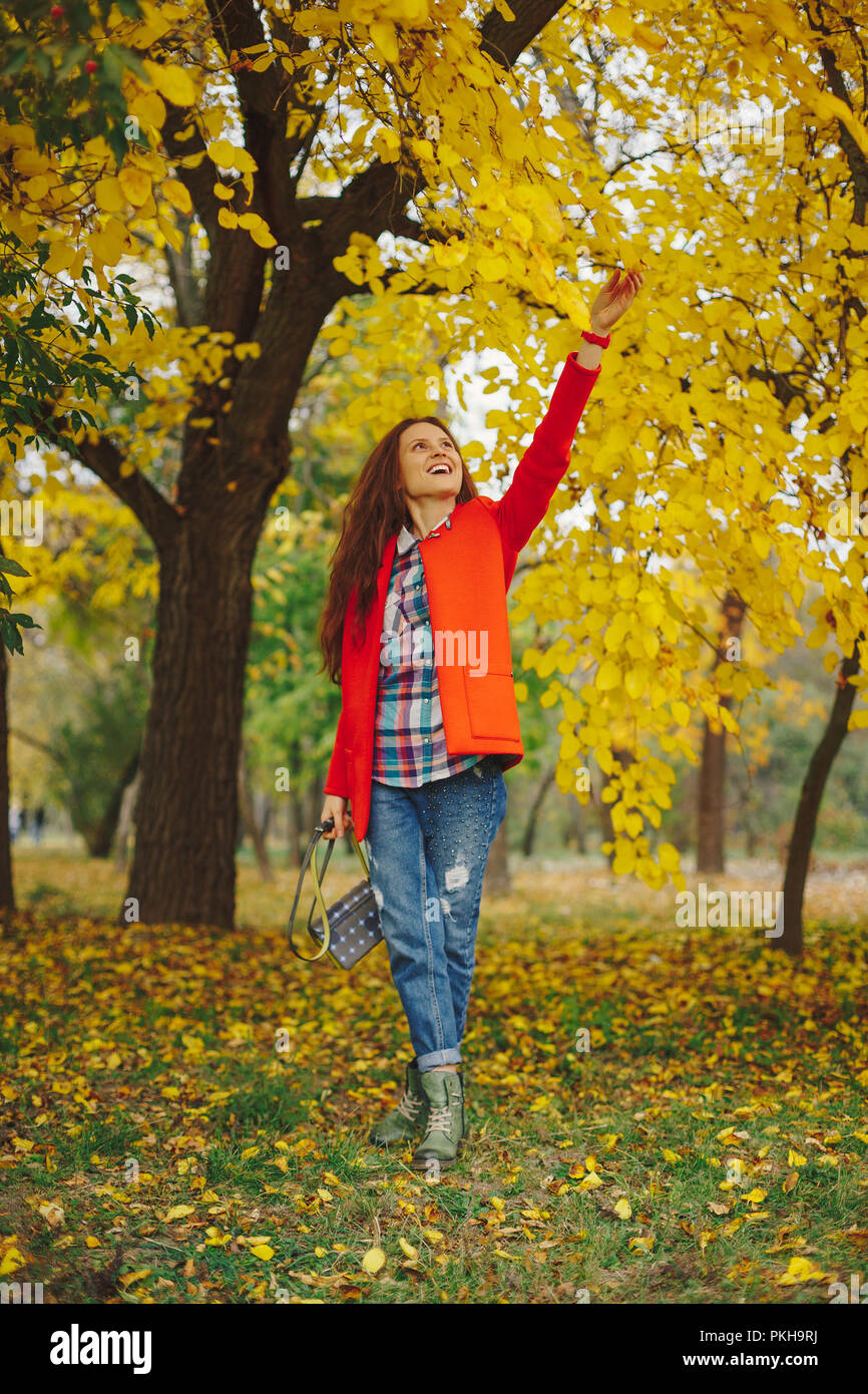 Felice ragazza con lunghi capelli ondulati godendo di Autunno nel parco. Bella giovane donna toccando foglie degli alberi in autunno park. Foto Stock