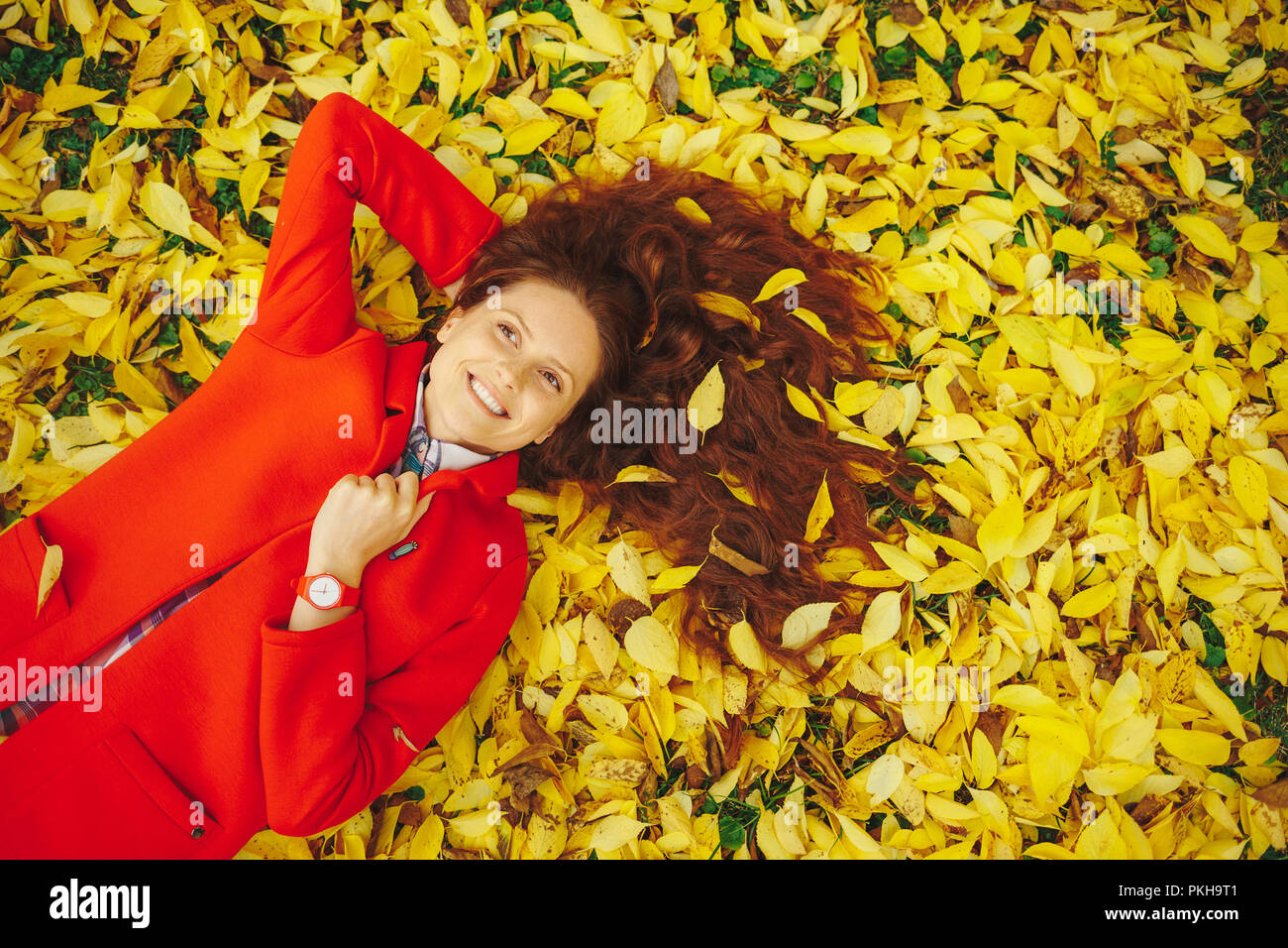 Bella ragazza felice con lunghi capelli ondulati decorato con foglie di giallo recante nella foresta di autunno holding umettare il collare con la mano. Allegro bella ragazza mi Foto Stock