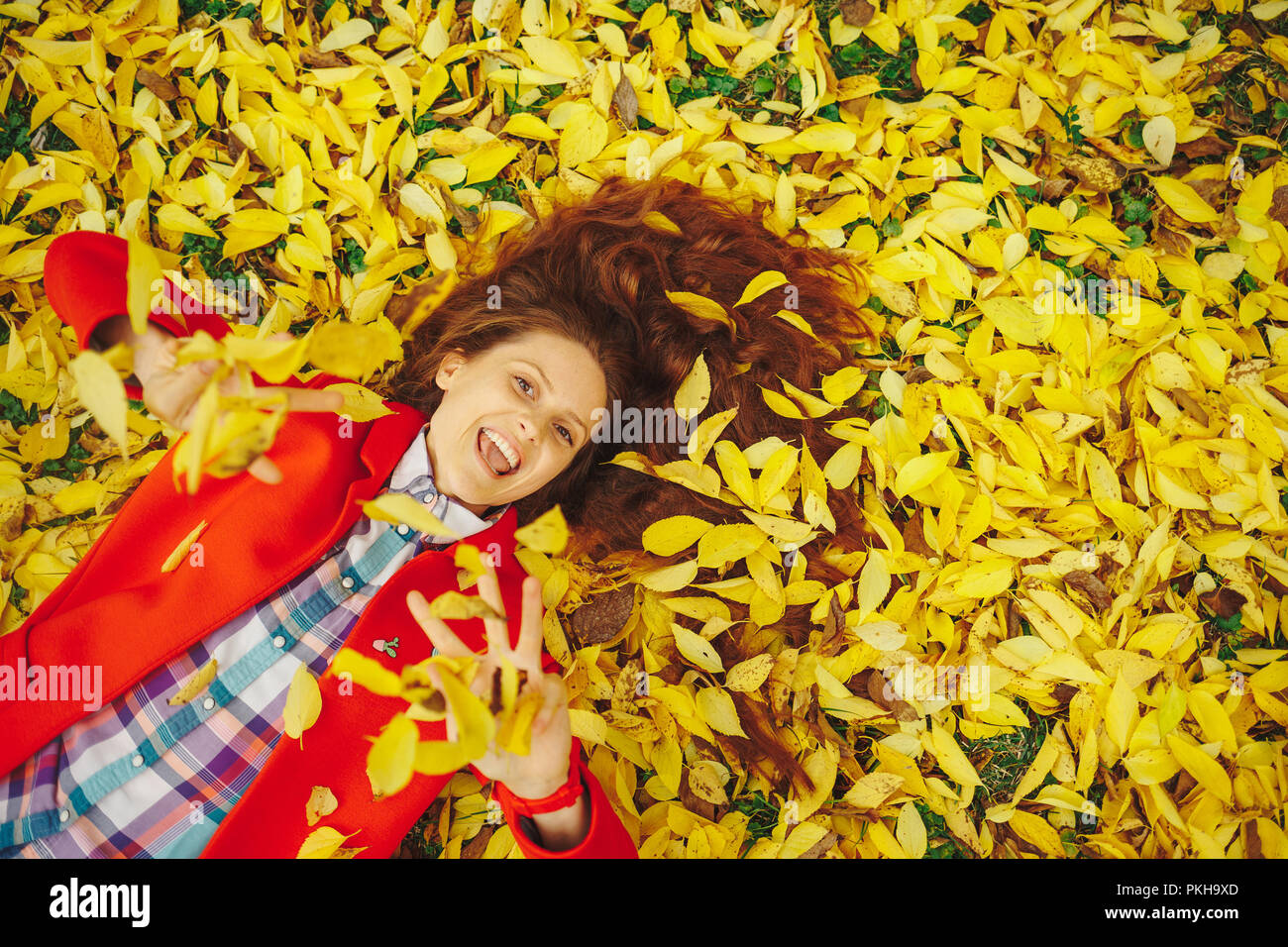In autunno le foglie che cadono sulla felice giovane donna nella foresta. Bella ragazza felice che stabilisce in giallo le foglie di autunno. Foto Stock