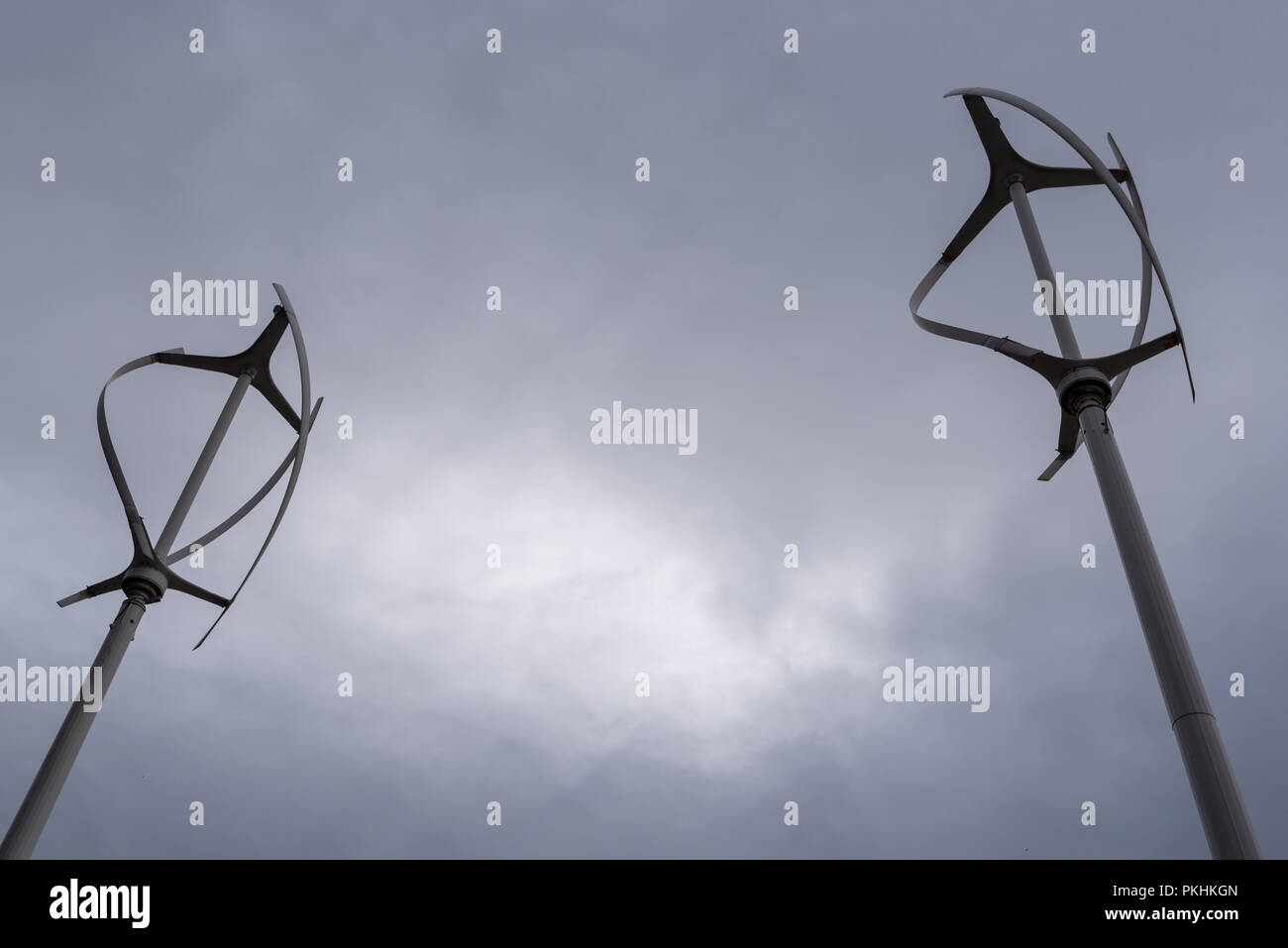 Asse verticale di generazione di energia eolica mulini con scuri nuvoloso nubi nel cielo che mostra futuro incerto di fonti di energia verde Foto Stock