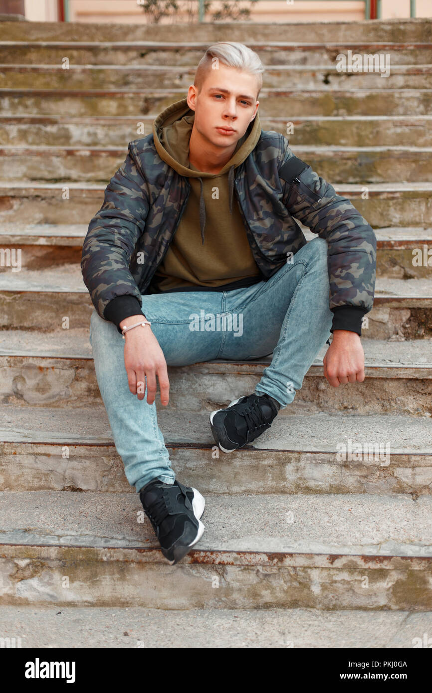 Elegante giovane uomo in una camicia militare con una felpa con cappuccio e  jeans in posa sui passaggi Foto stock - Alamy