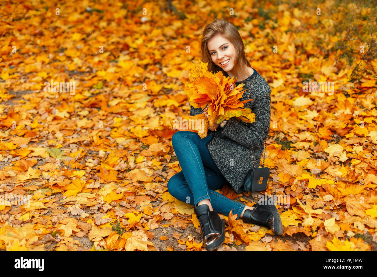 Bella donna felice con un sorriso in un quartiere alla moda di rivestire godendo il momento in autunno il fogliame giallo. Buon umore Foto Stock
