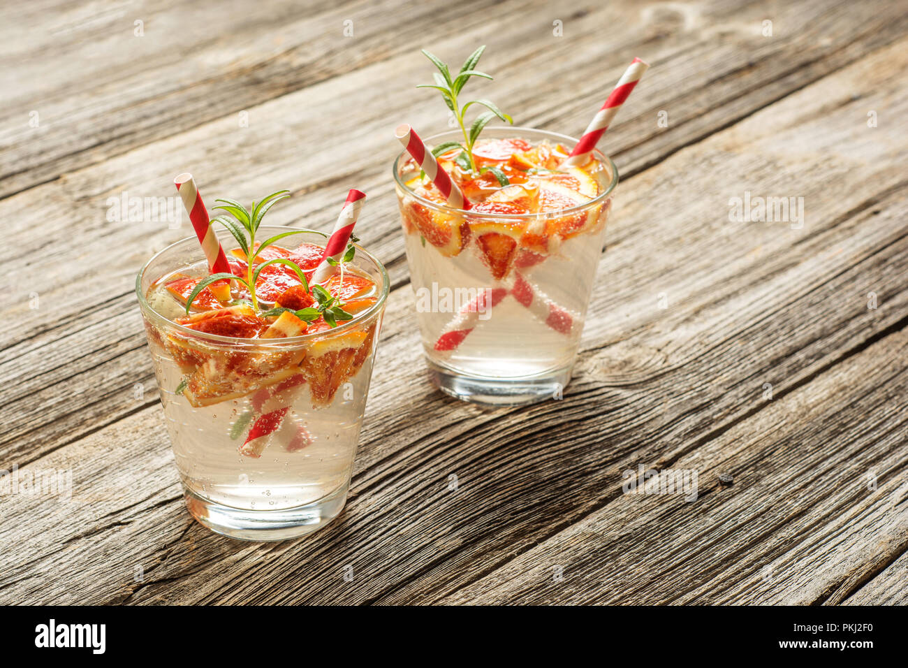 Due bicchieri di bevanda rinfrescante con arancia e rosmarino in legno rustico sfondo . Concetto di ricetta, cocktail. Foto Stock