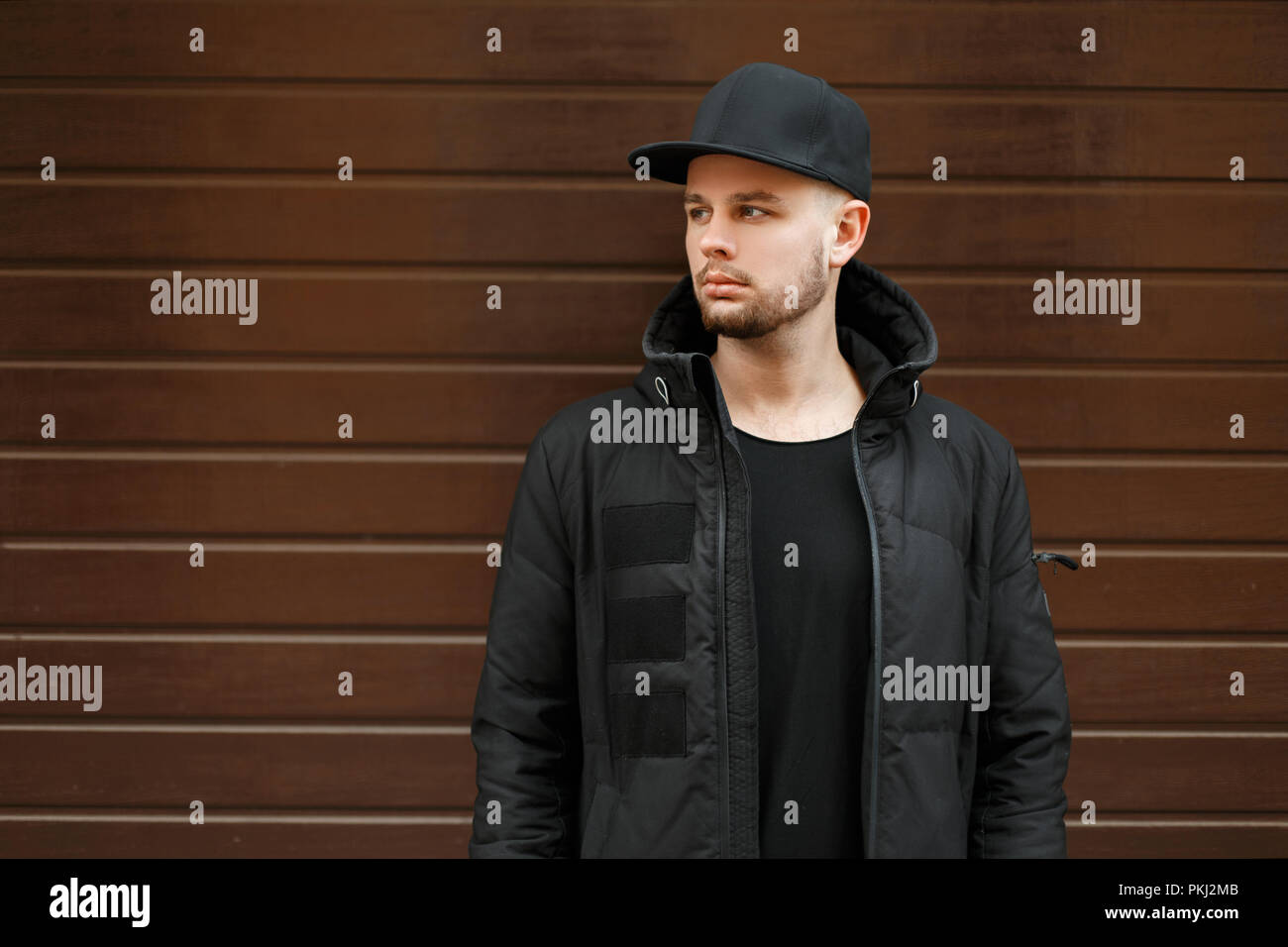 Bel giovane hipster uomo in un nero elegante berretto da baseball e giacca  invernale sorge in prossimità della parete Foto stock - Alamy