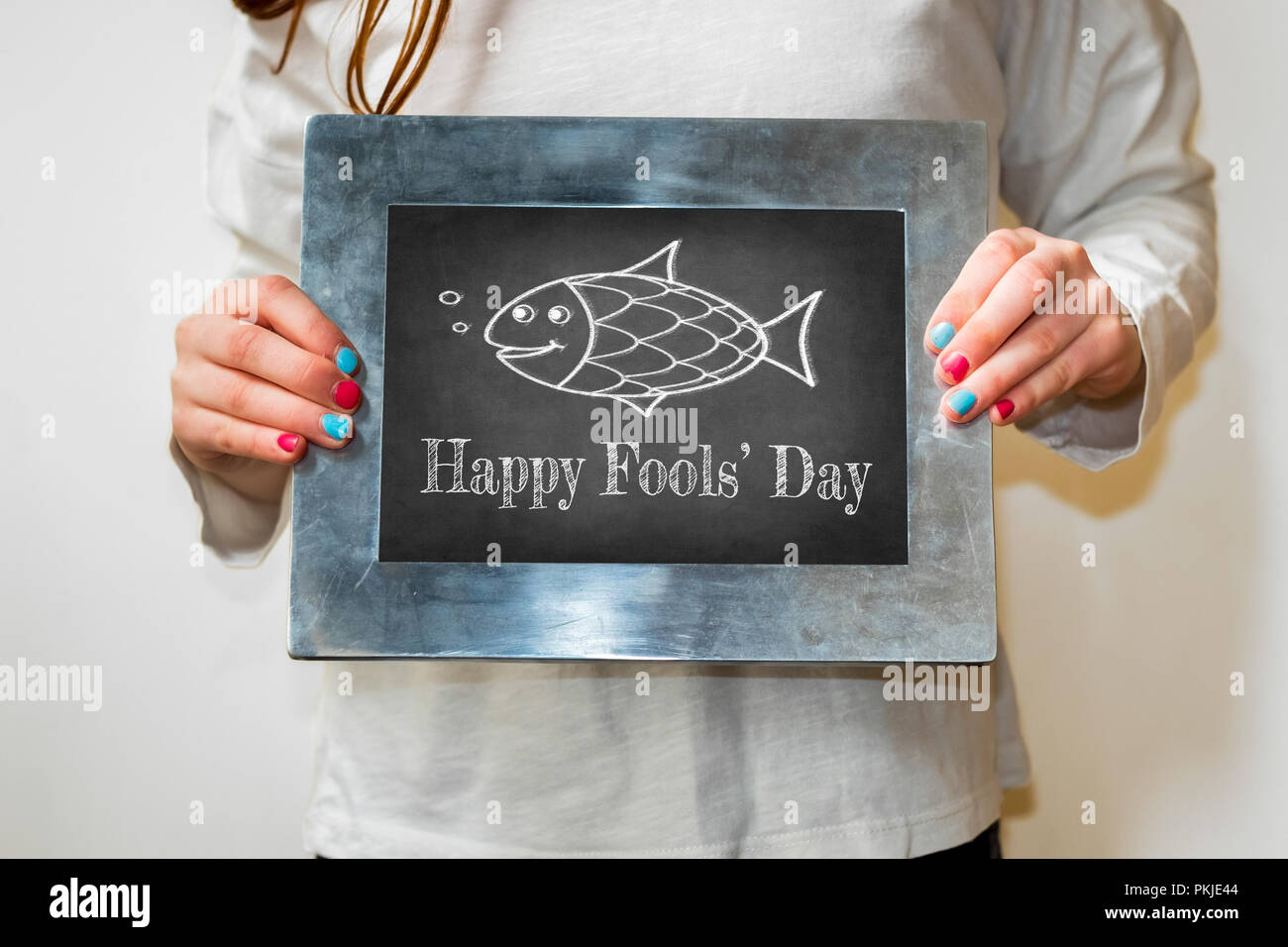 Ragazza giovane azienda fino a blackboard con testo happy fools day e pesce Foto Stock